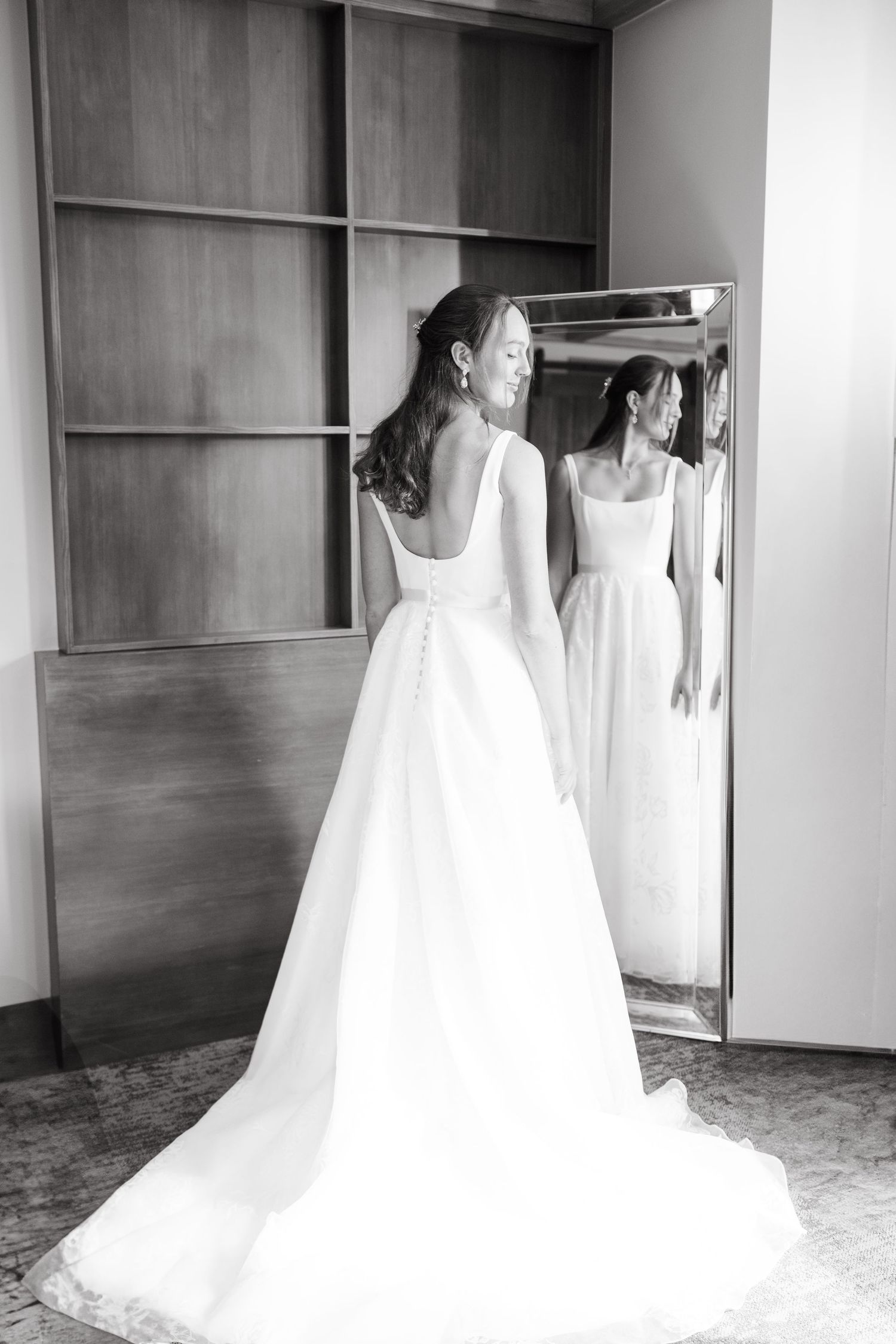 A white wedding dress with a flowing train displayed in front of a mirror in an elegant dressing room.