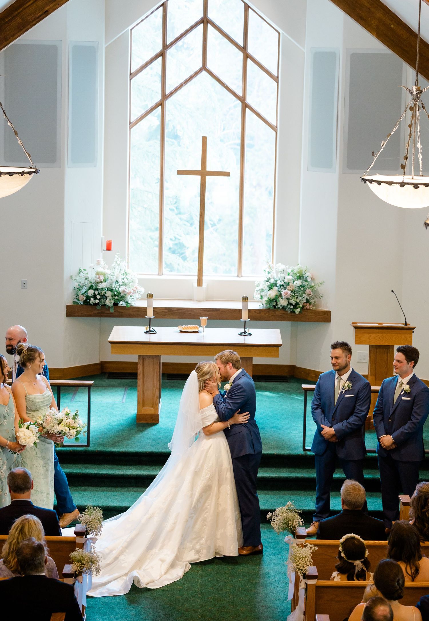 Wedding ceremony in progress inside modern church with large windows and wooden beams overhead.