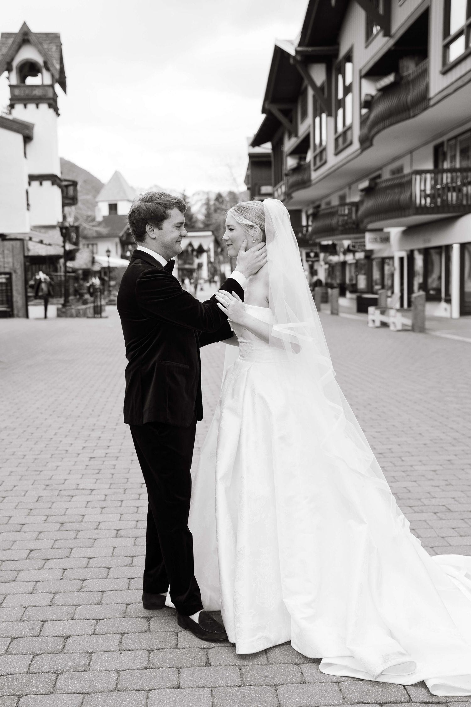 Bride and groom share a tender moment on a cobblestone street, with the groom gently holding her face.