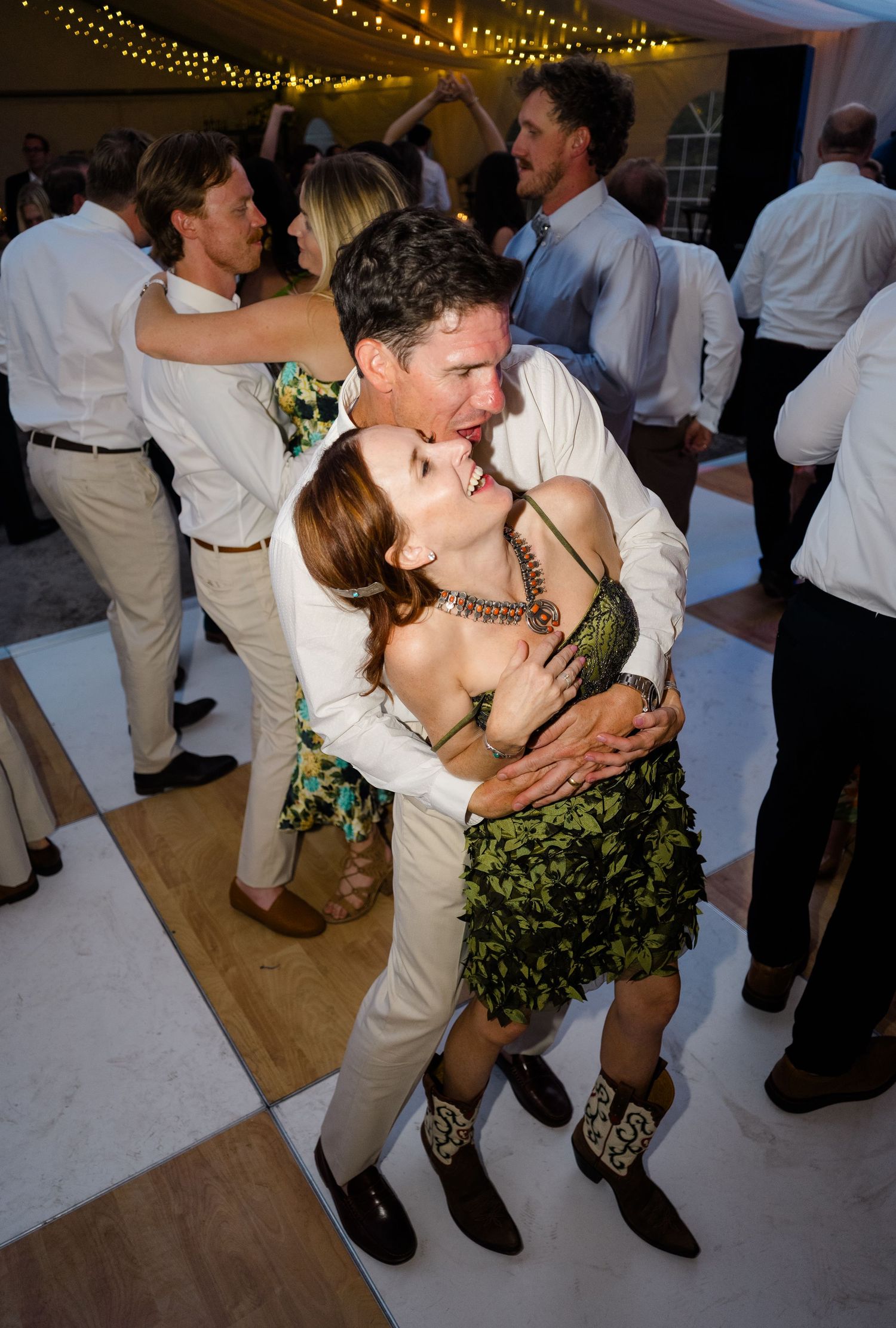 Couples dancing and embracing joyfully at an elegant indoor wedding reception with string lights.