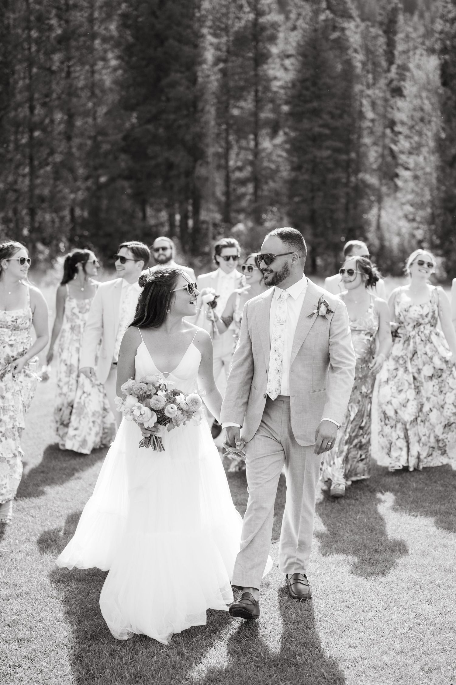 Black and white photo of wedding party walking through a wooded path.