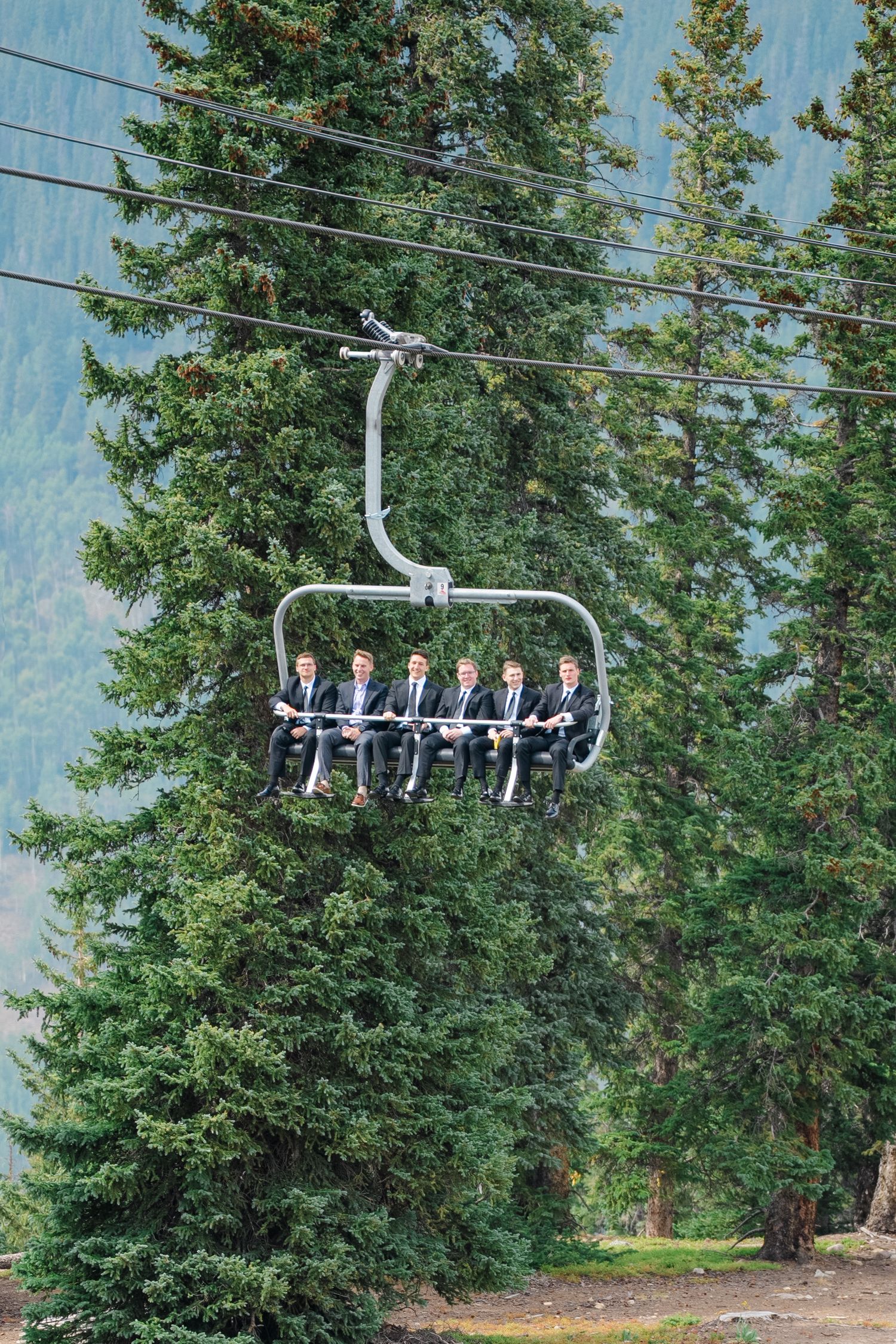 Ski lift chairs glide past evergreen trees against a blue sky on a sunny mountain day.