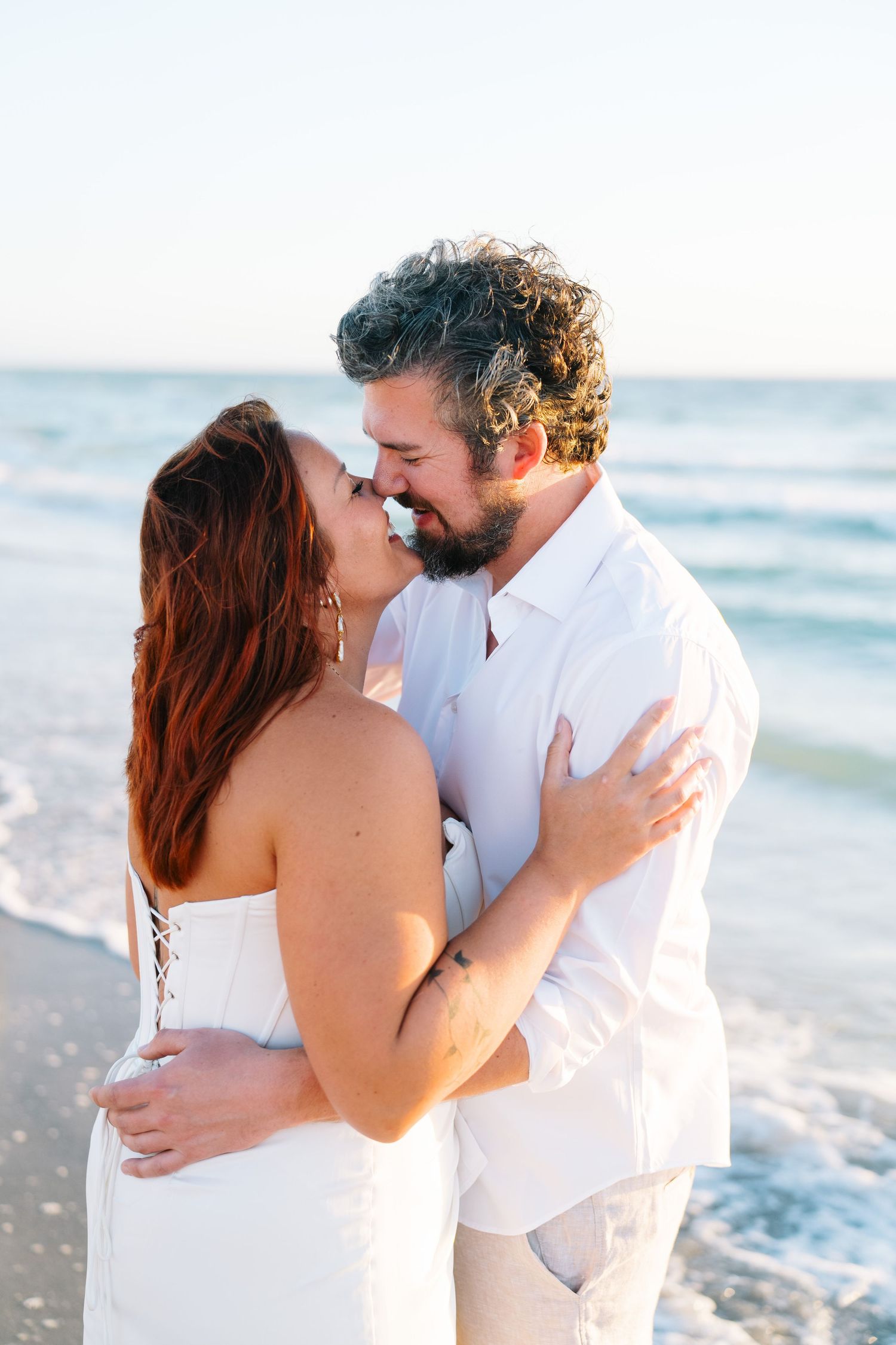 Close up of couple embracing on beach with turquoise ocean waves in background.