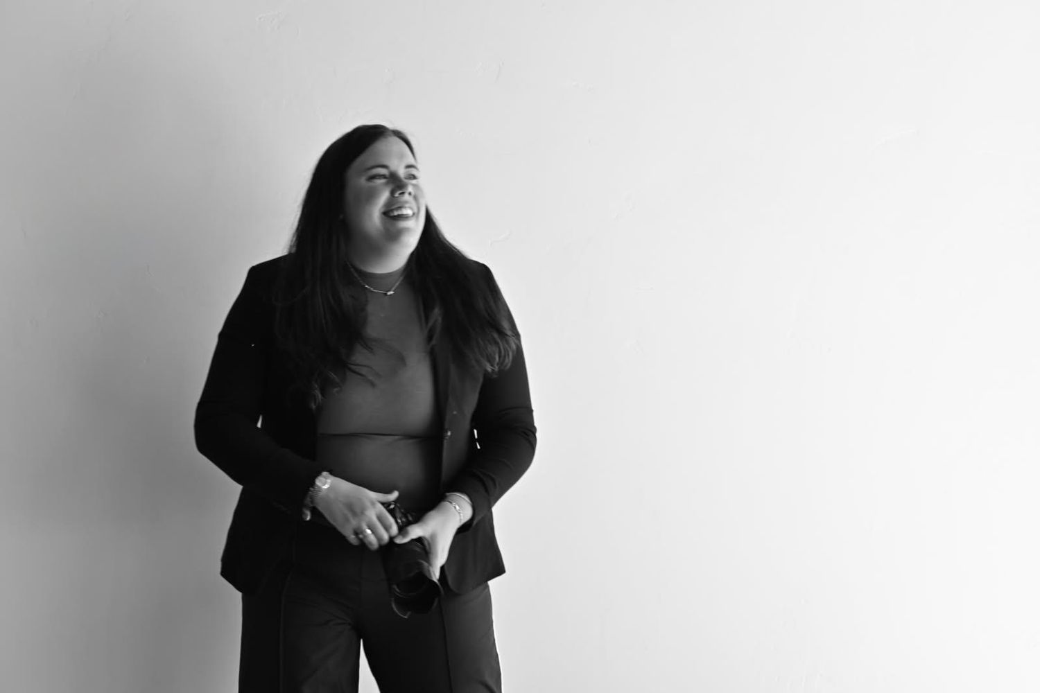 Breckenridge wedding photographer wearing a black jacket stands against a light background while gesturing and laughing.