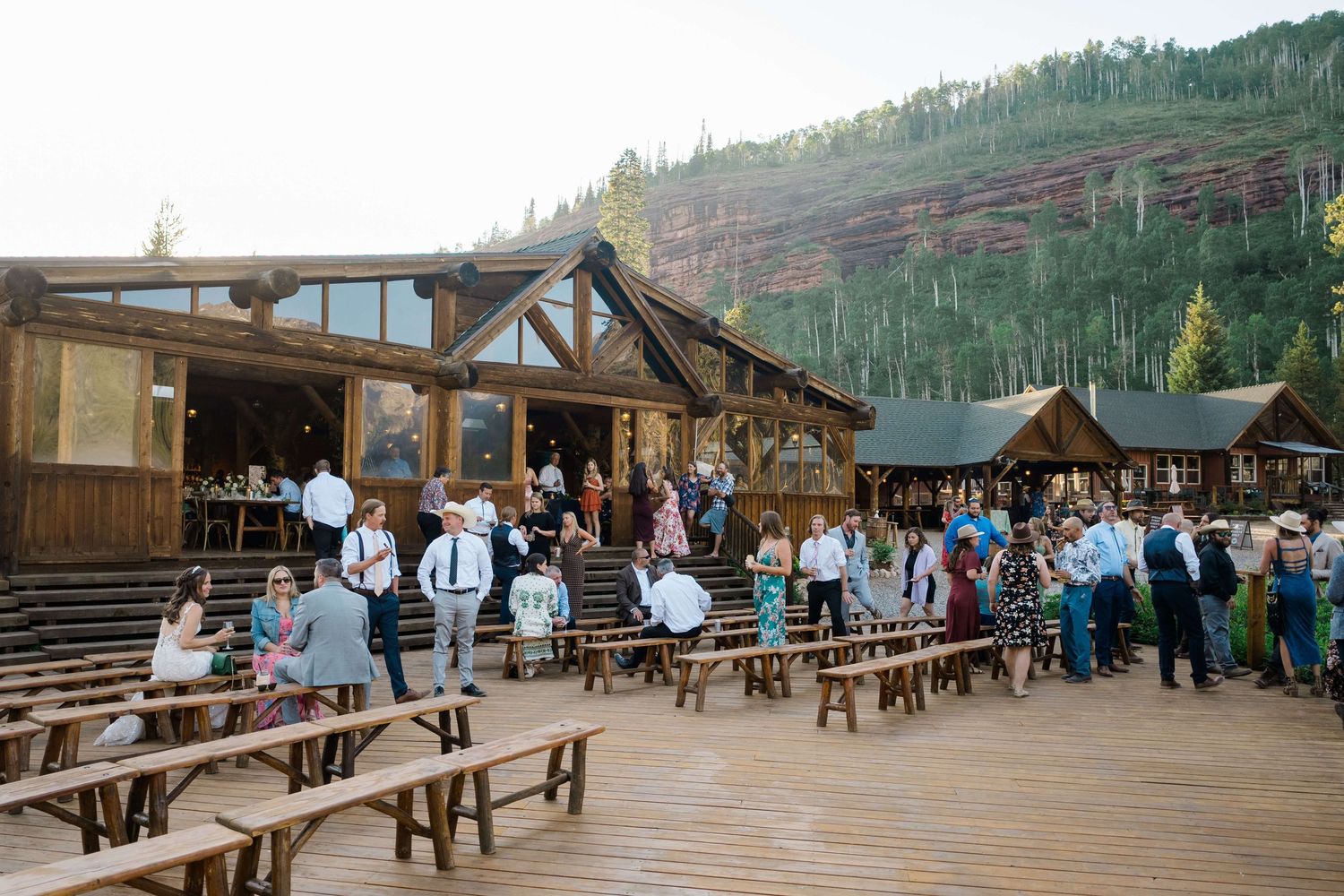Guests mingle on a rustic wooden deck at a mountain lodge wedding venue surrounded by evergreen trees Piney River Ranch Vail Wedding