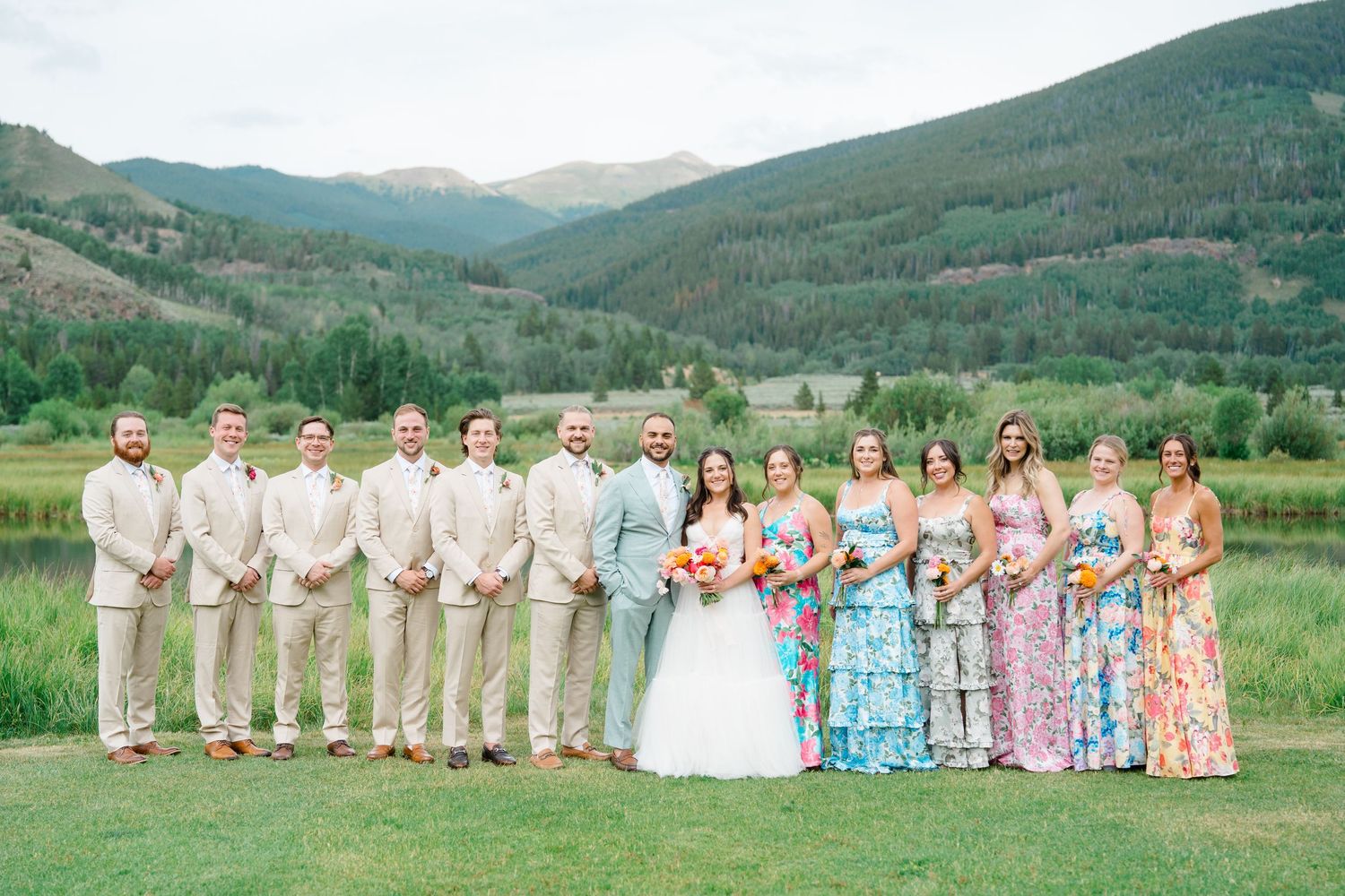 Wedding party poses together against scenic mountain backdrop in Colorado with bridesmaids in floral dresses.