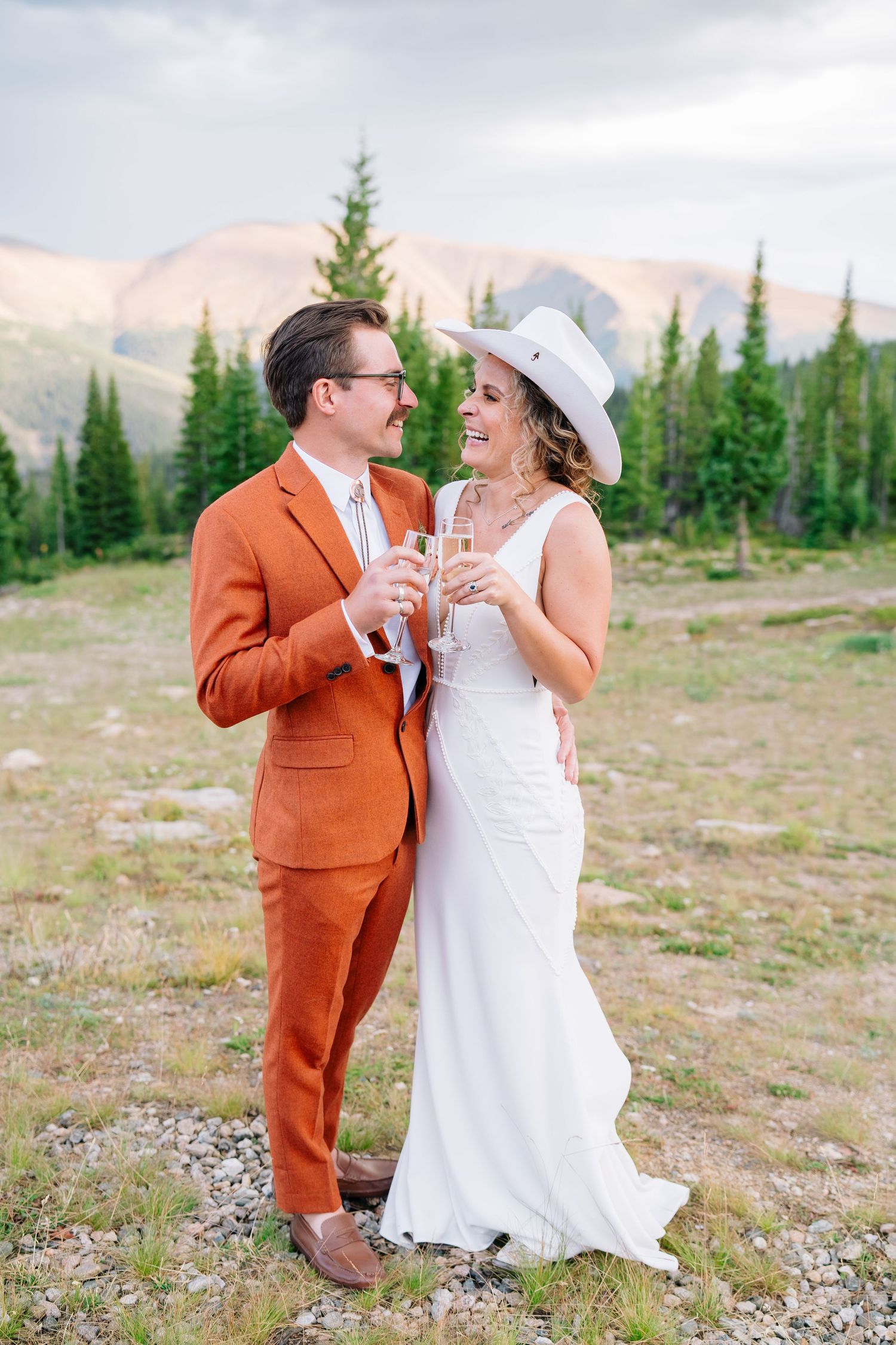 Vail, Colorado Wedding Photographer captures couple in orange suit and white dress sharing playful moment in mountain setting.