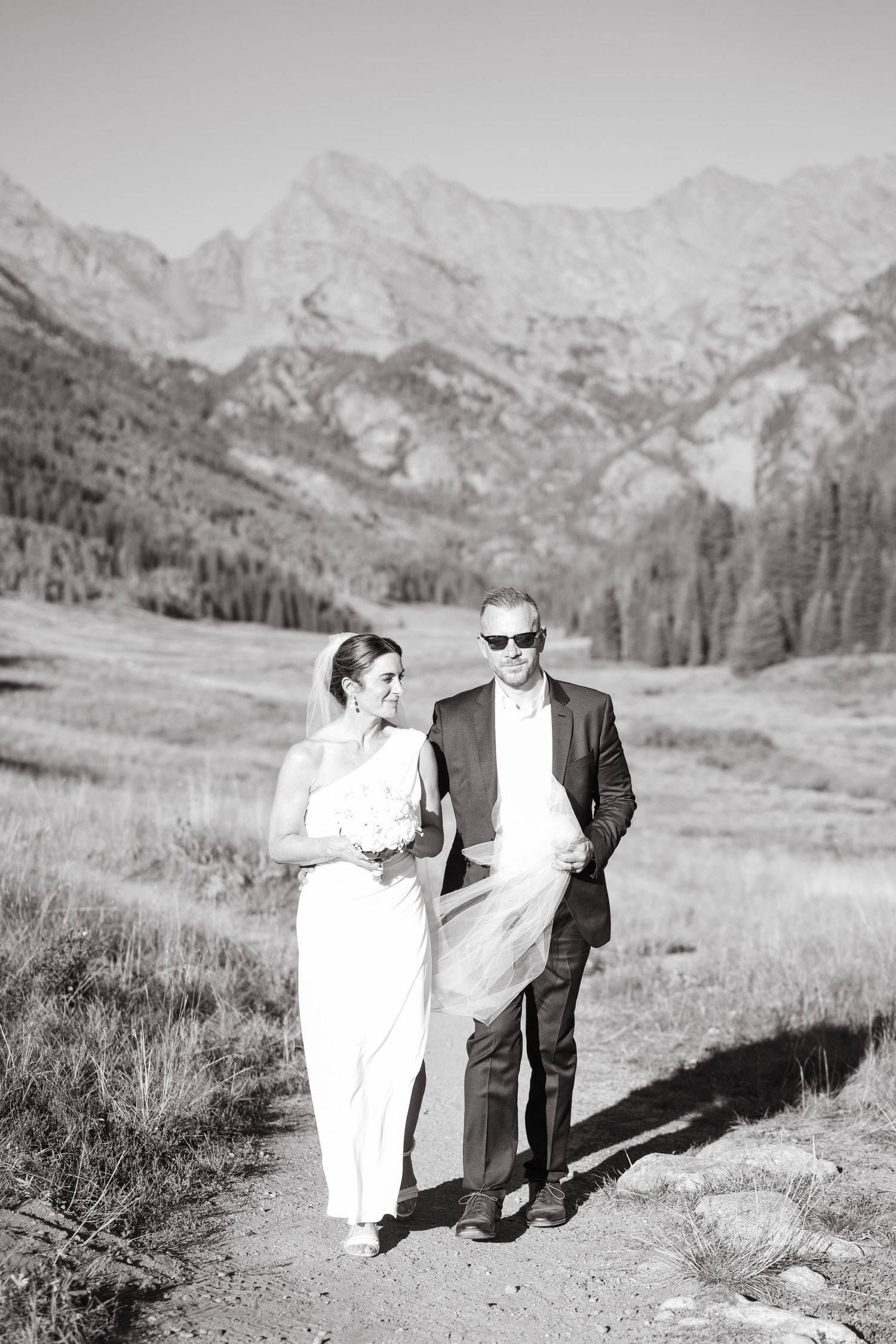 Black and white wedding photos showing couple walking together in scenic mountain meadow landscape during piney river ranch elopement.