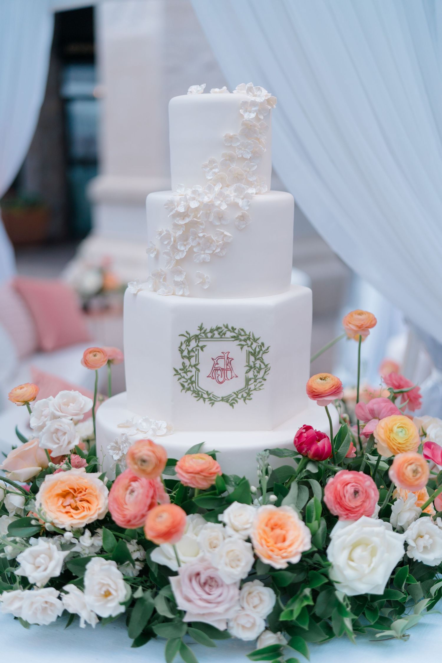 Elegant white tiered wedding cake adorned with delicate pearls and surrounded by peach and pink roses on display.