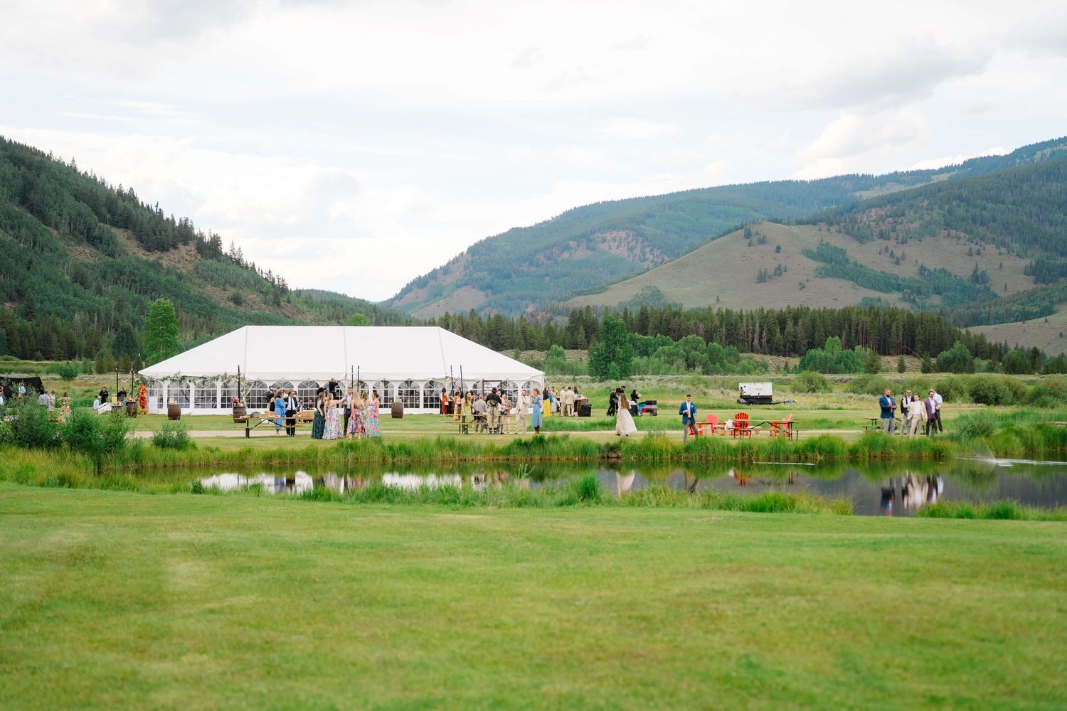At Camp Hale Wedding Venue - Elegant outdoor wedding reception tent set against lush green mountains and a serene pond in a valley setting.