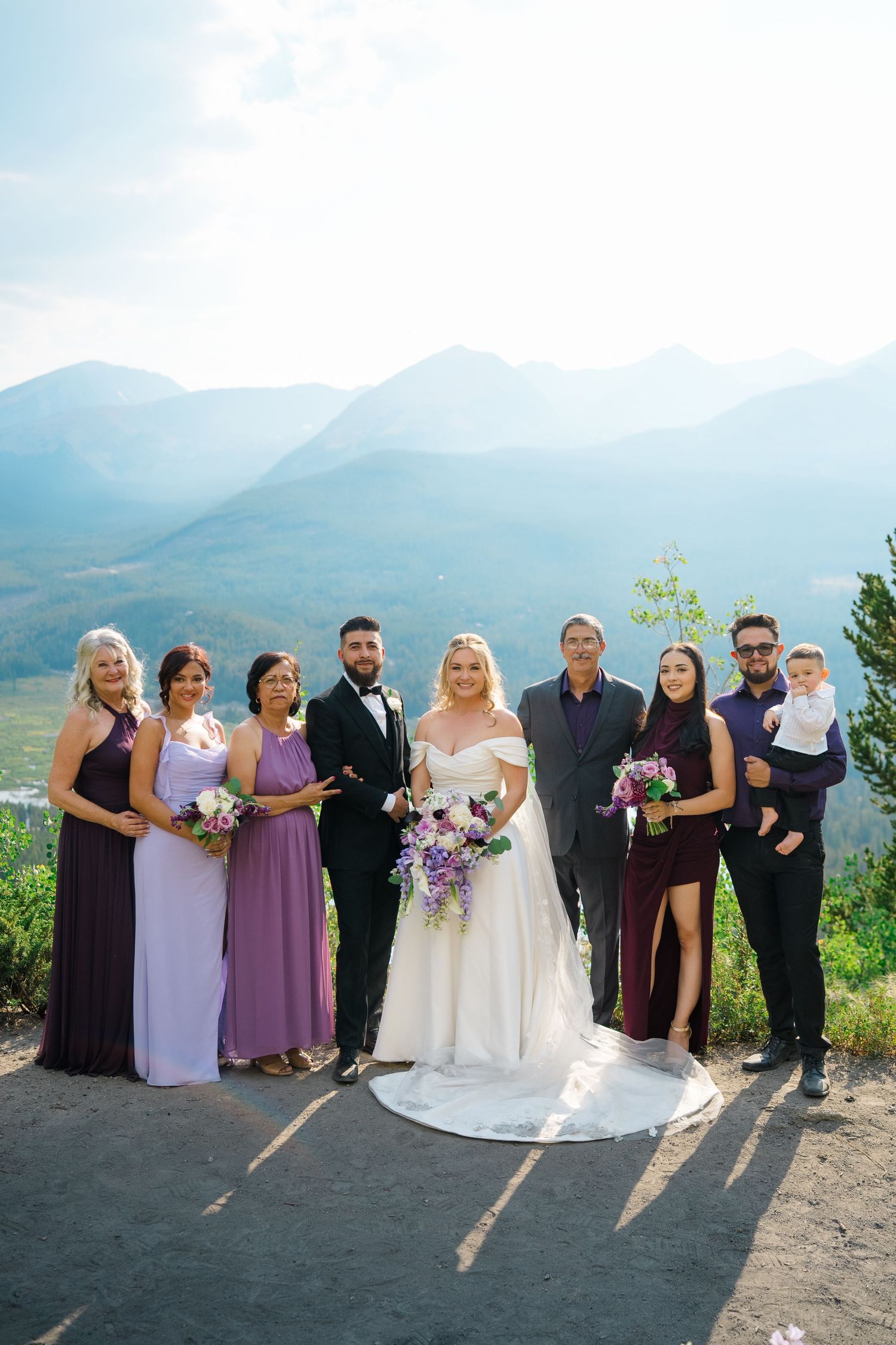 Wedding party poses together on scenic mountain overlook with purple and white attire against dramatic landscape during Breckenridge wedding