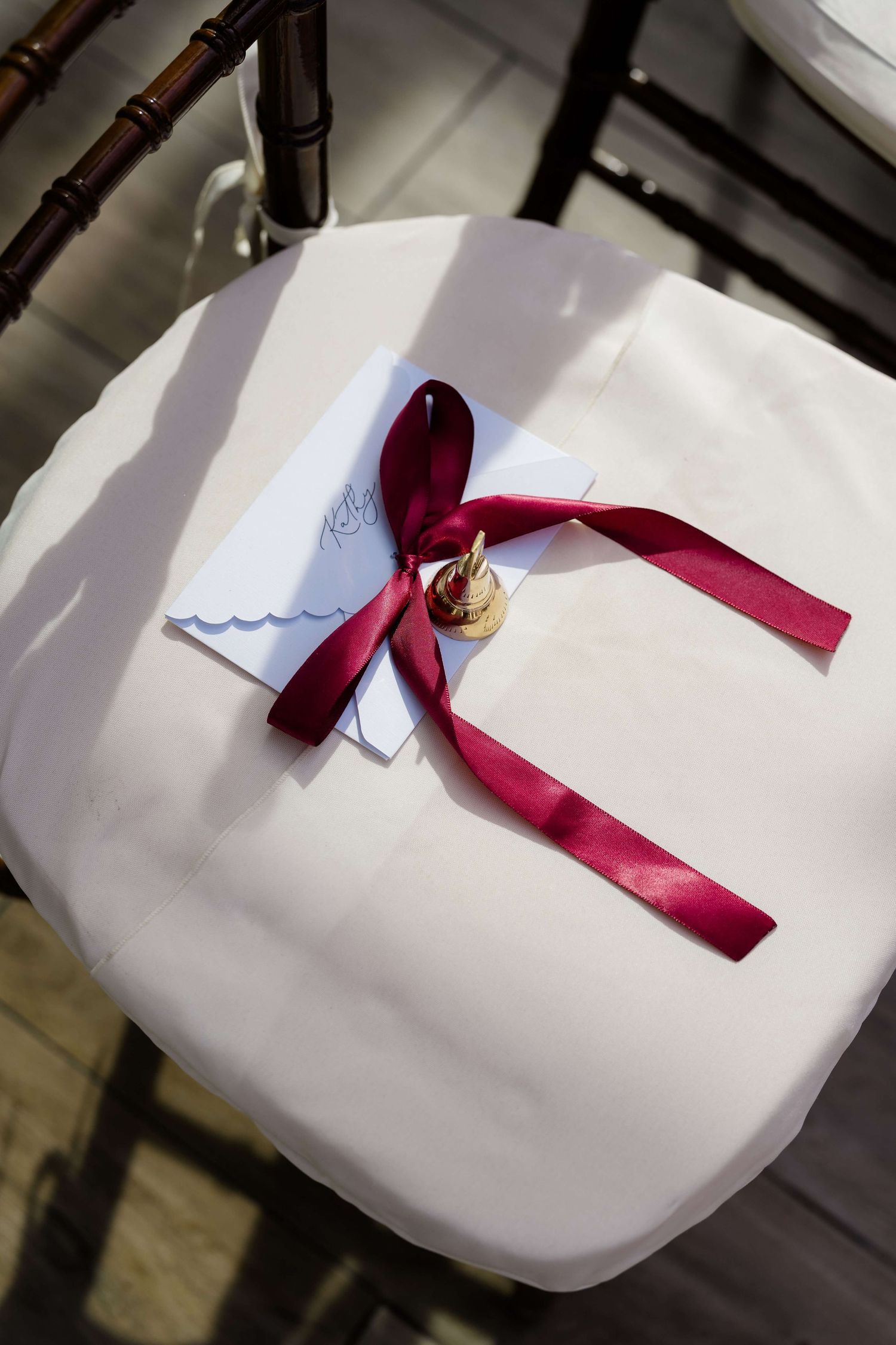 Elegant wedding program tied with a burgundy satin ribbon and gold wax seal on a white chair cushion.