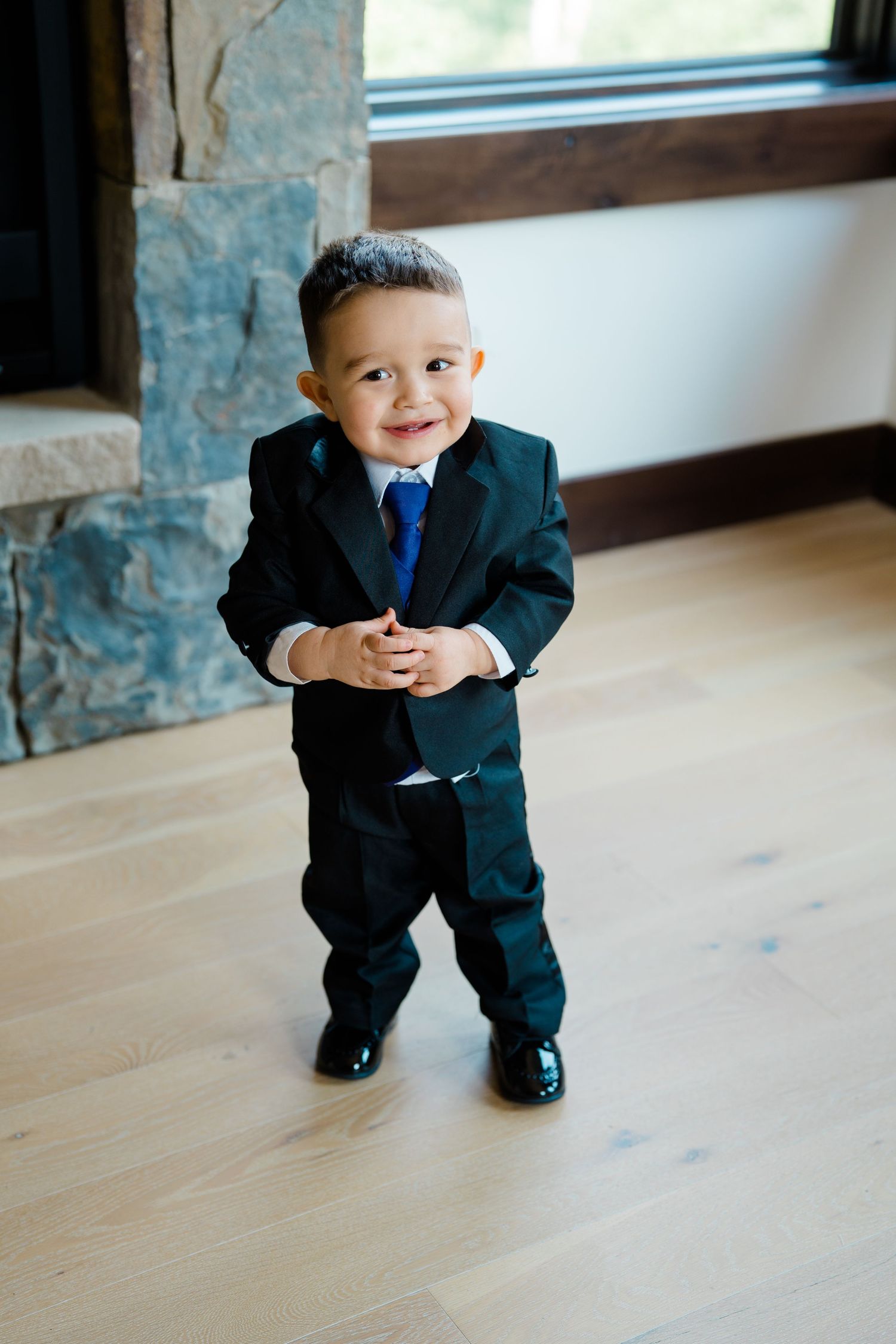 Small child in formal suit strikes adorable poses on wooden floor.