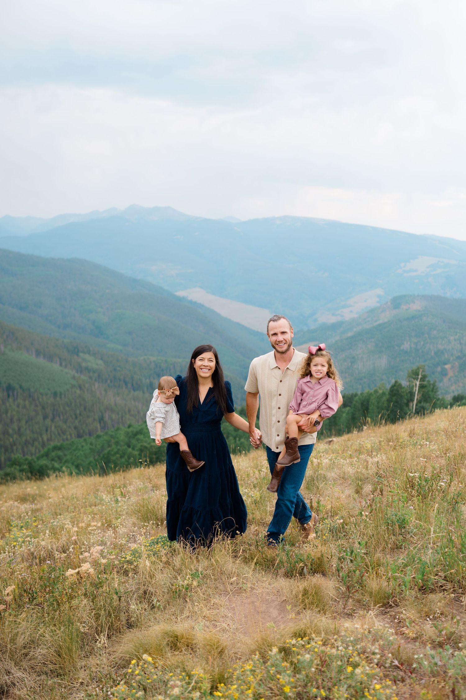 Family group walking and playing together on mountain trail with scenic valley views during vail mountaintop family photography session.
