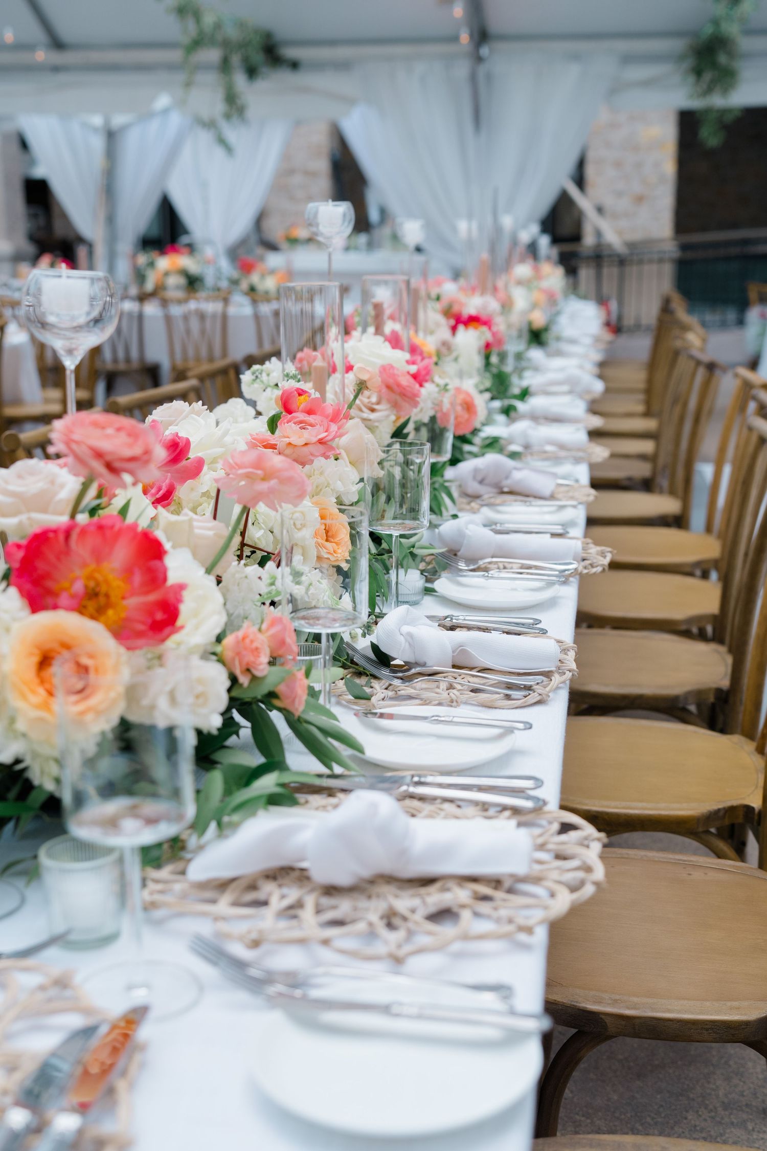 Elegant wedding reception tables set with white linens, gold chairs, and coral and peach floral centerpieces.