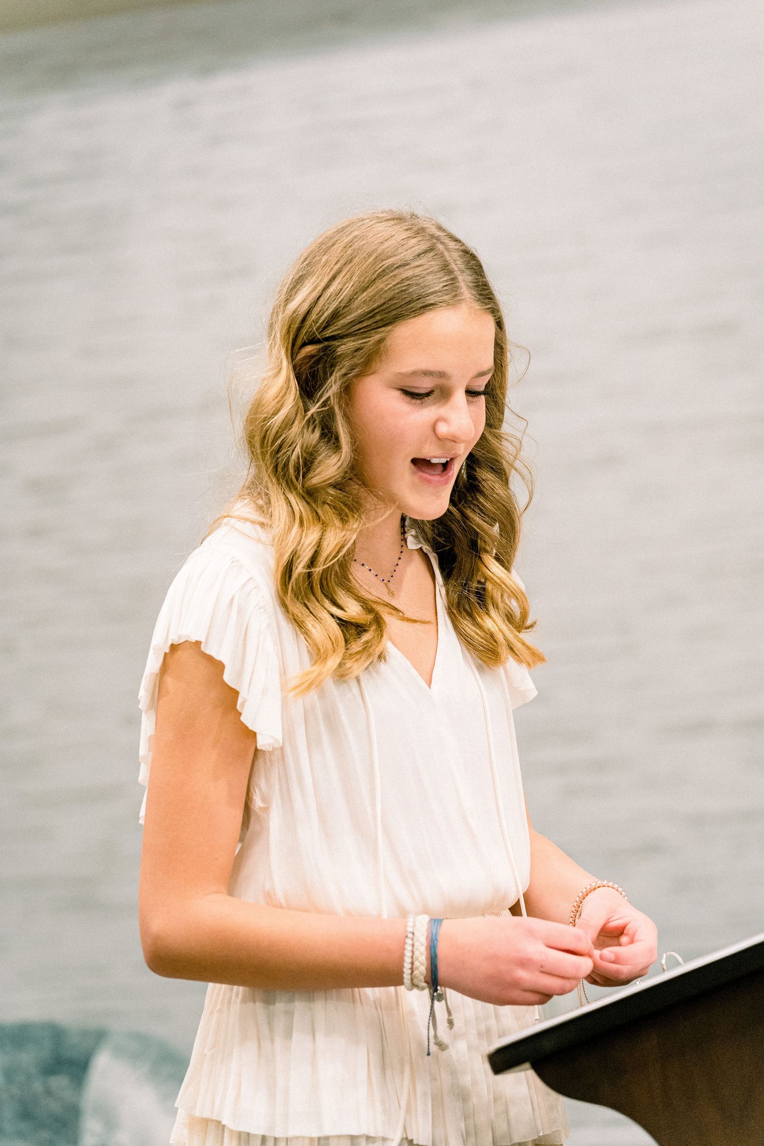 A person in a white dress looking down at papers on a podium during a ceremony.