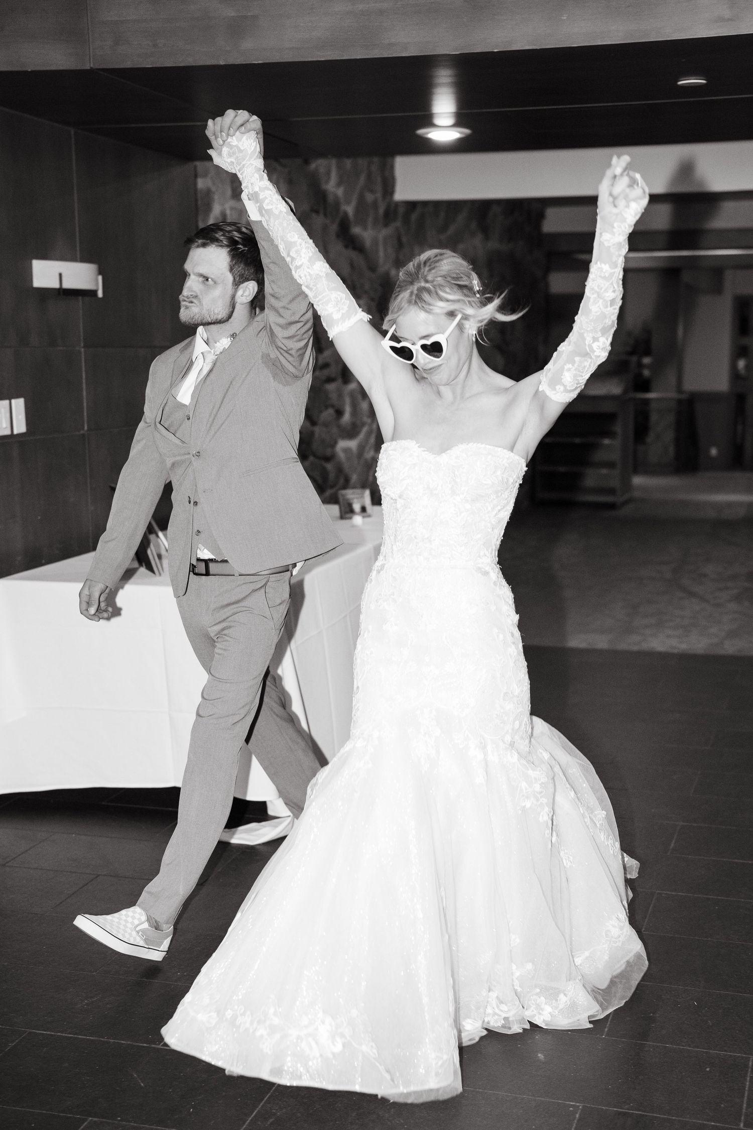 Black and white photo of newlyweds celebrating with raised arms on the dance floor.