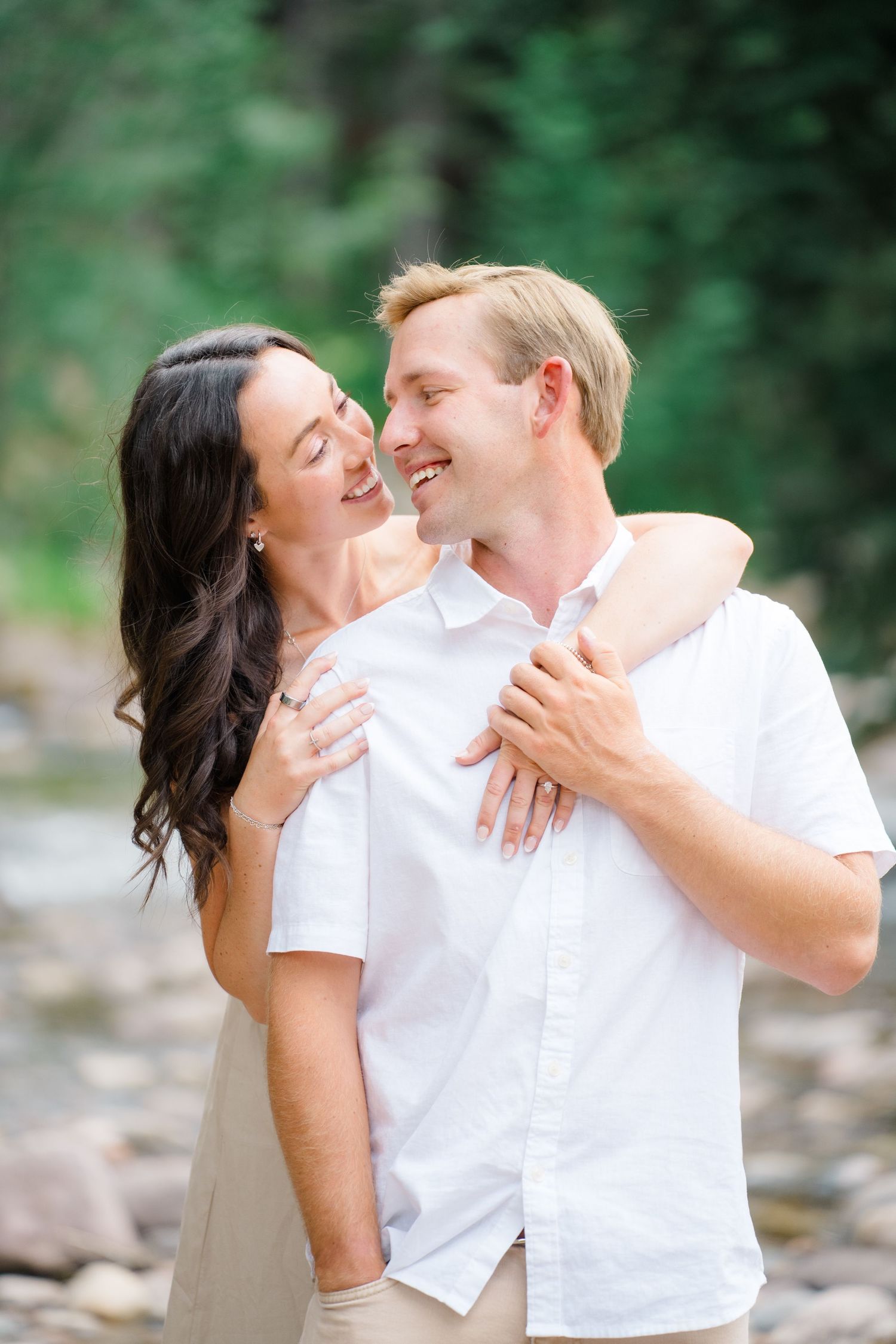 A couple shares joyful laughter and tender moments in a series of romantic outdoor photos with green foliage background.