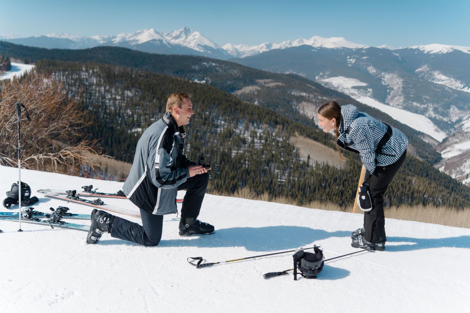 A person snowboarding down a snowy mountain slope with scenic mountain peaks in the background.