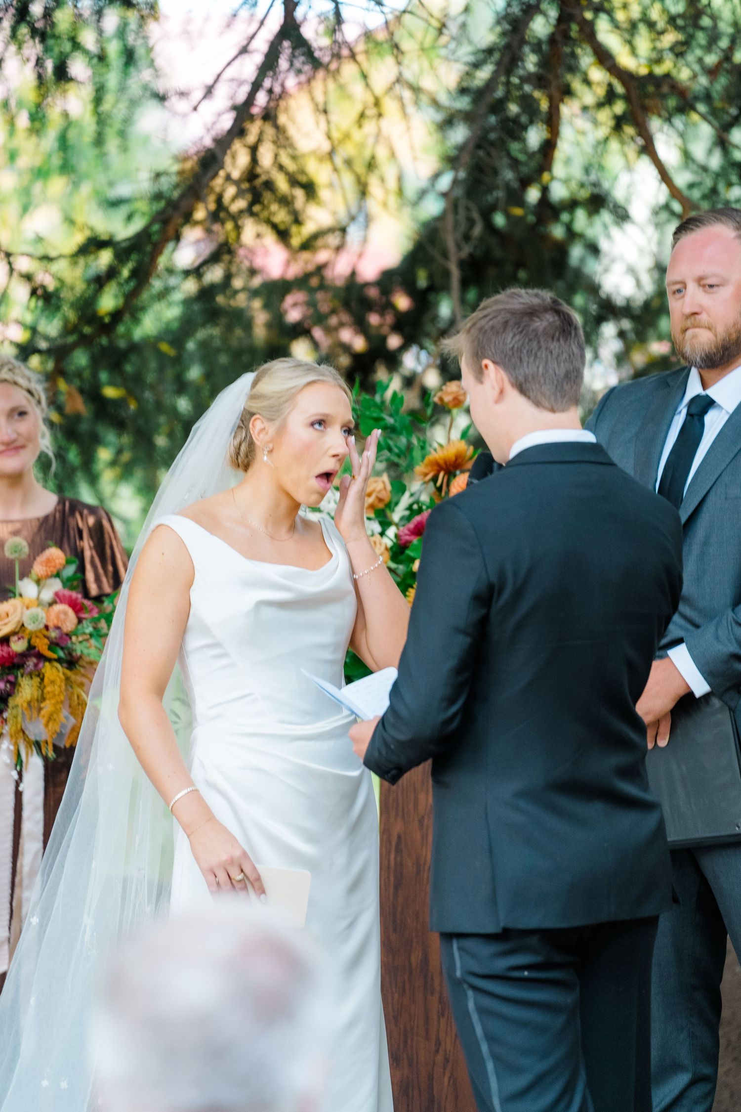 A wedding ceremony moment under evergreen trees with the wedding party looking on.