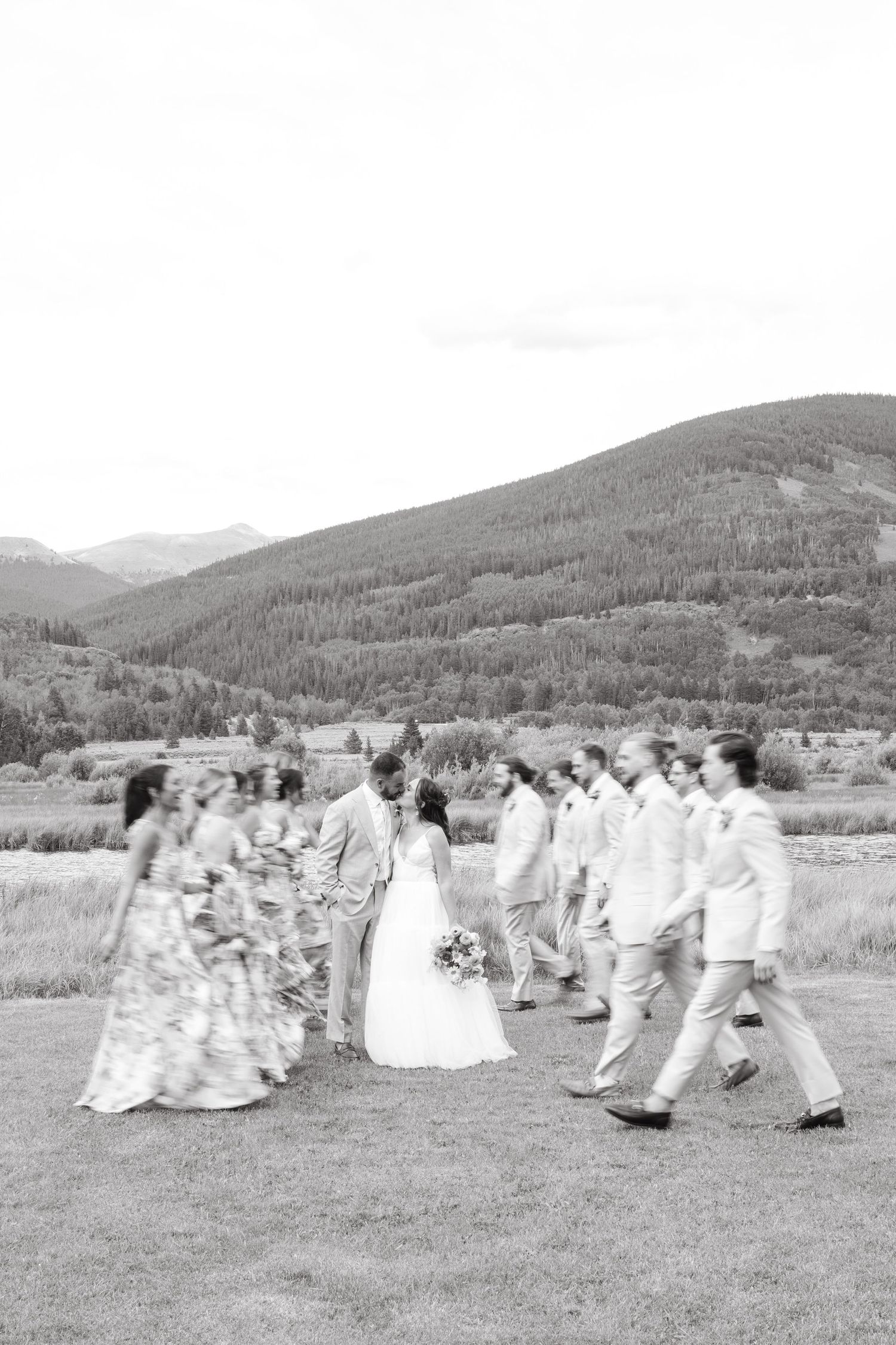 Wedding party poses together on a grassy hillside in black and white photography.