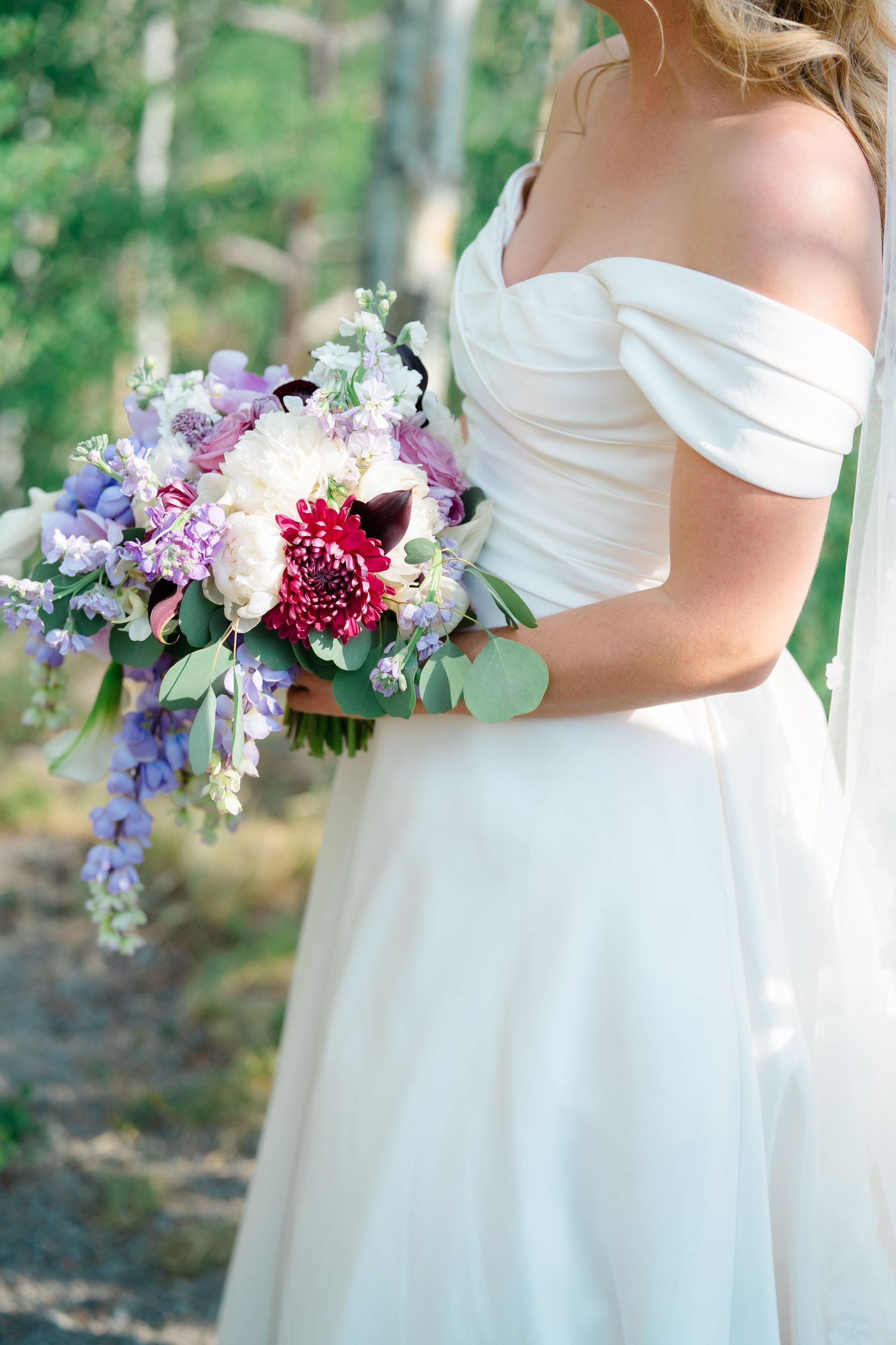 Close-up of a bridal bouquet featuring purple and white flowers against a white wedding dress.