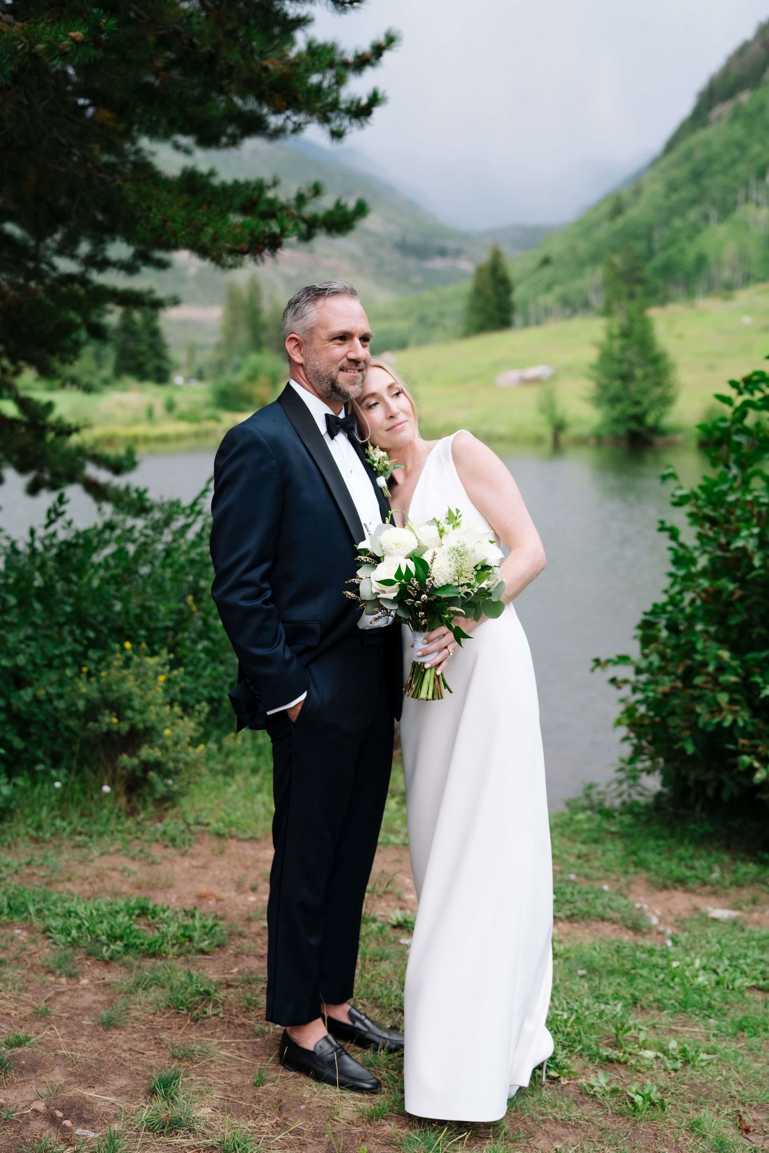 At Vail Golf Club Vail Wedding Venue -  Bride and groom pose together near a mountain lake