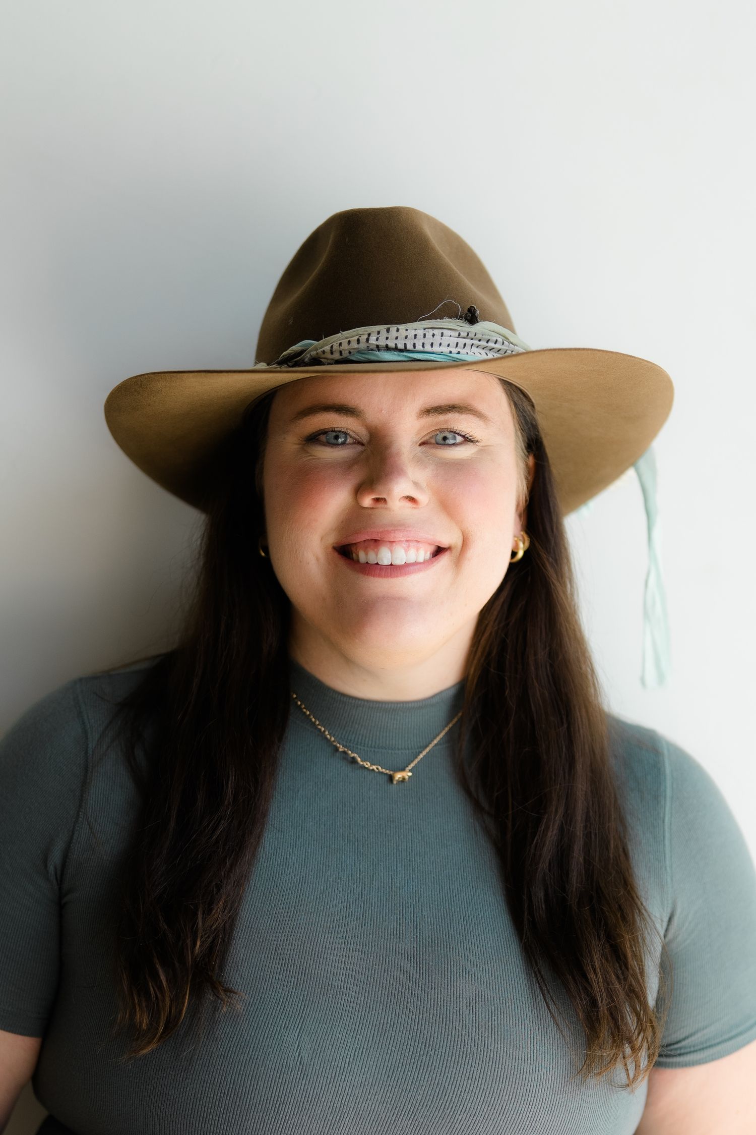 Vail Colorado Photographer Sierra Sturt - Portrait series showing someone in western hat and grey shirt smiling against white wall.