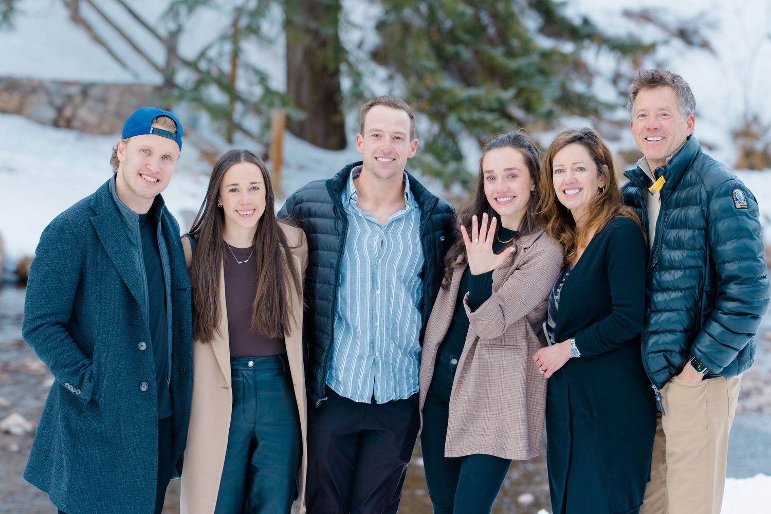 A group poses together in a winter setting with snow and evergreen trees in the background.