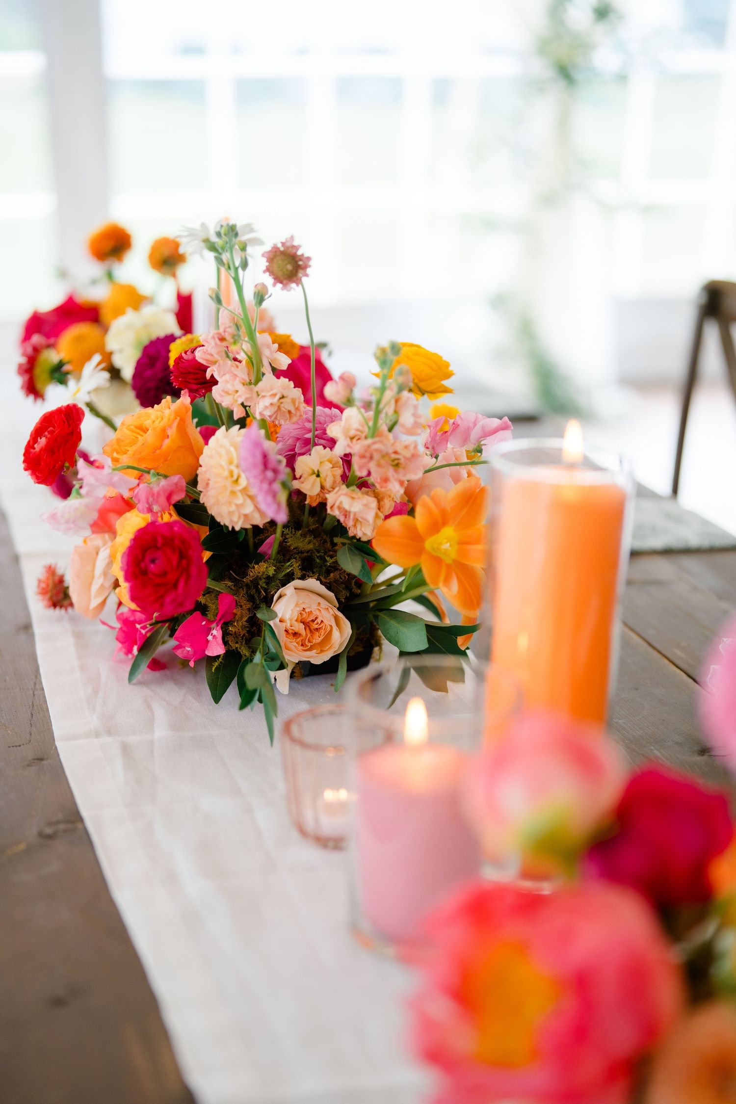 Elegant table setting with vibrant pink and orange flower arrangements and glowing candles.