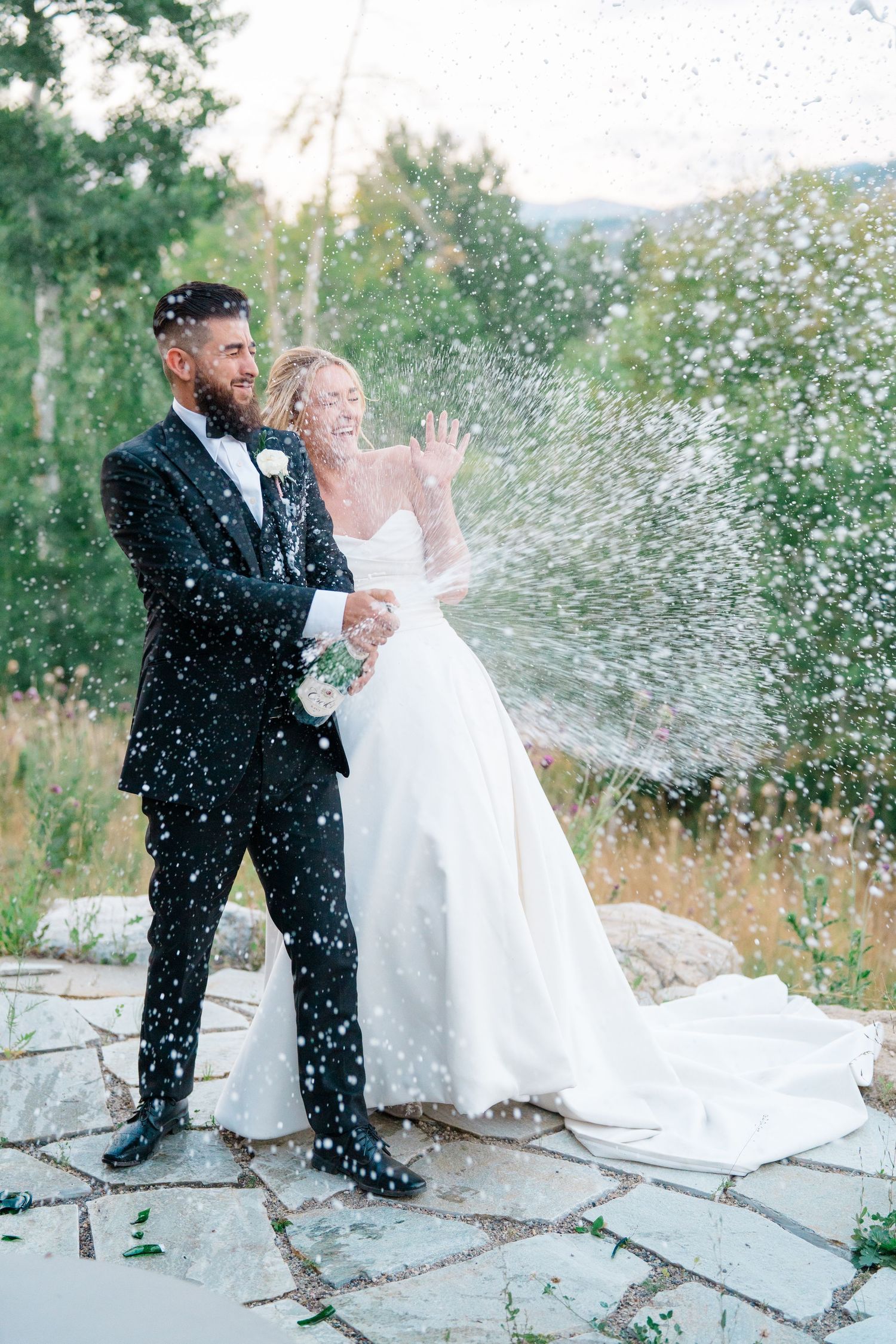 A fun wedding photo sequence showing champagne being sprayed and celebrated outdoors on stone steps.