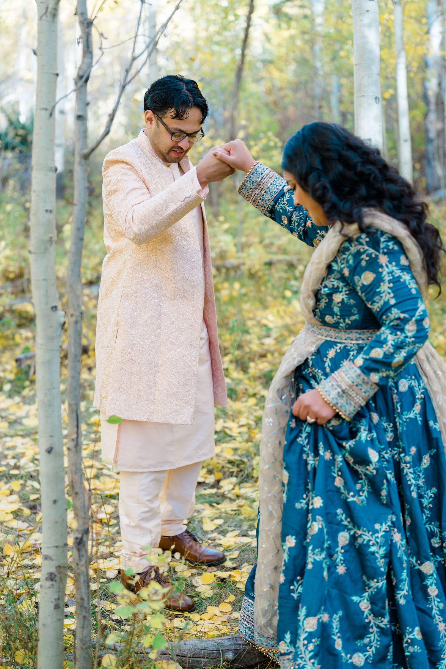A couple in pink and blue outfits share tender moments together in a sunlit aspen forest during autumn.