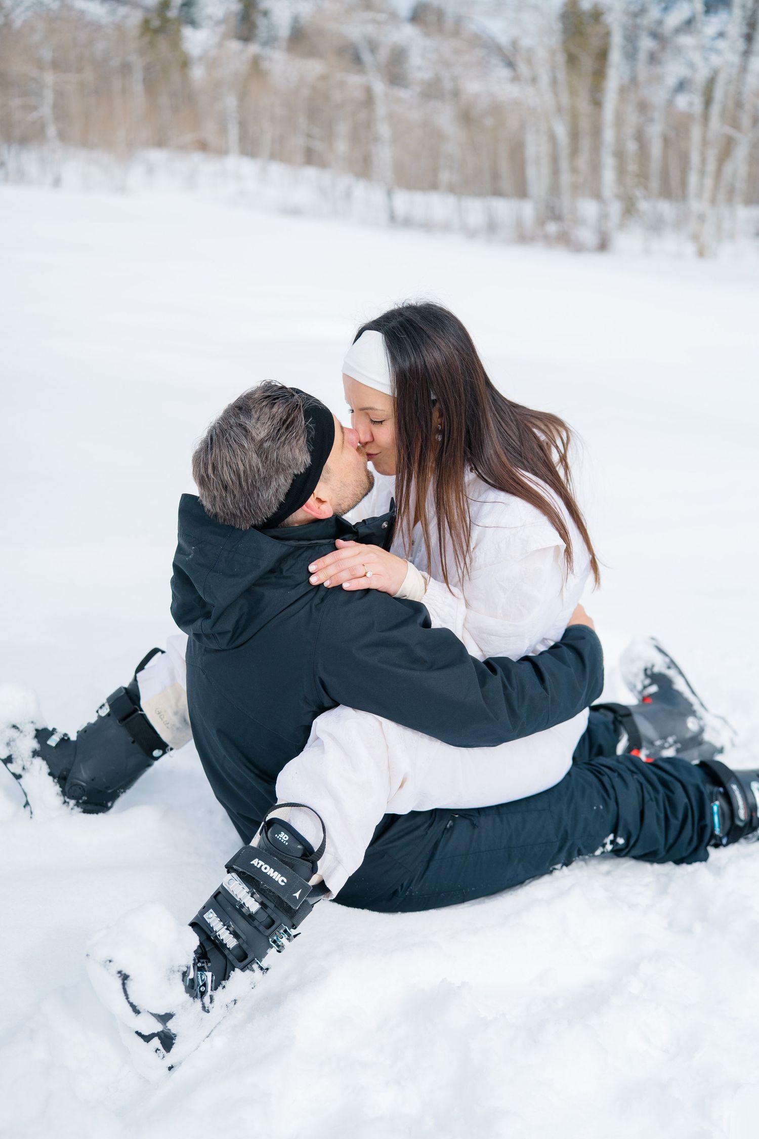 Two people in winter clothing playfully roll in fresh white snow during a winter photoshoot.