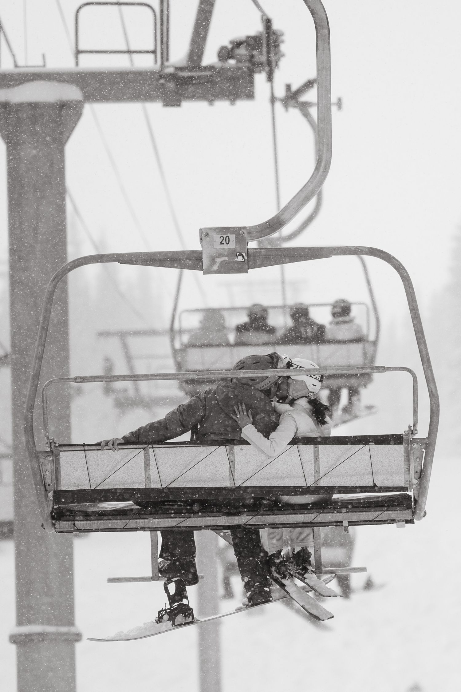 Black and white photo of skiers riding a chairlift up a snowy mountain slope.