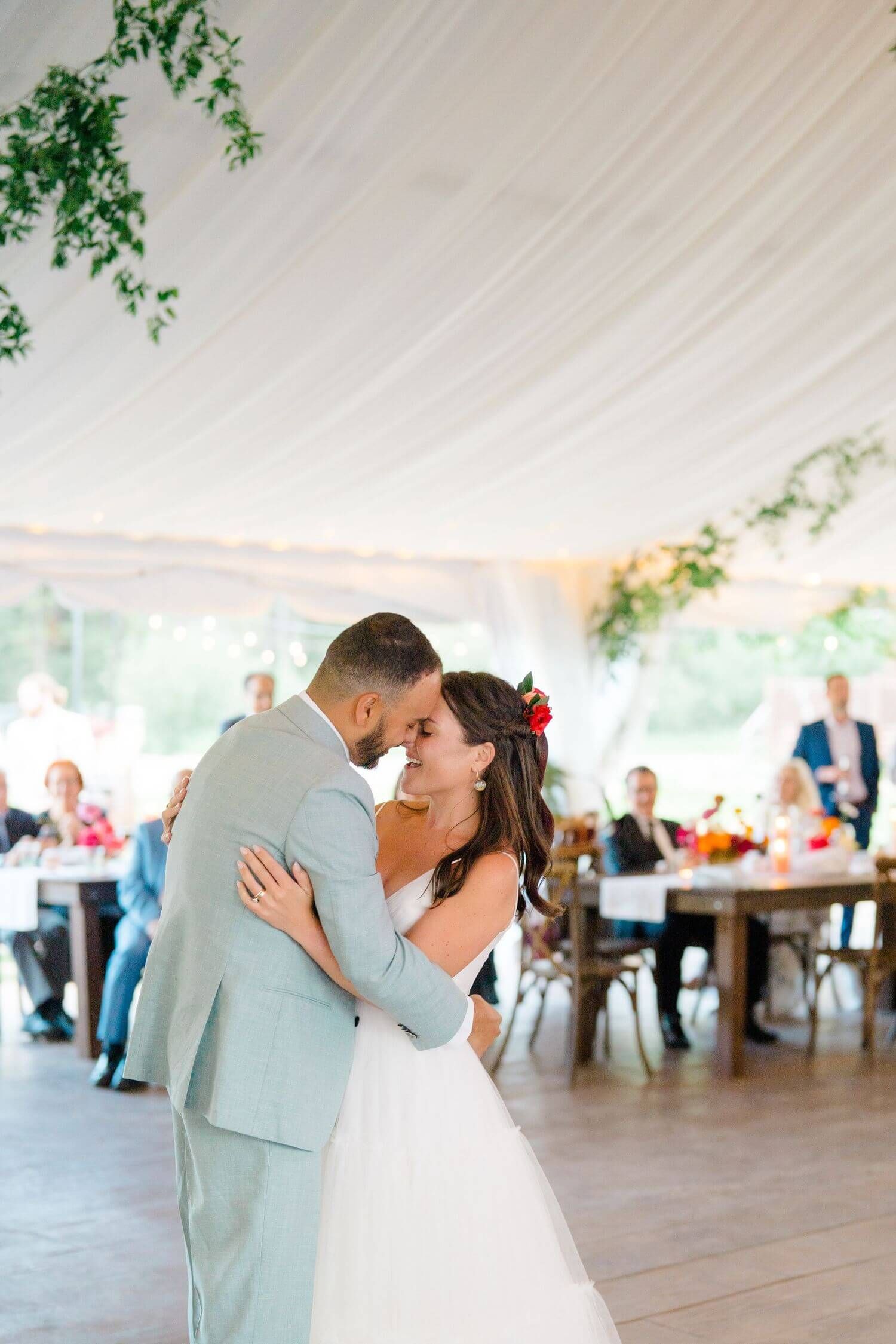 A romantic first dance moment under a white tent decorated with hanging greenery at Camp Hale.