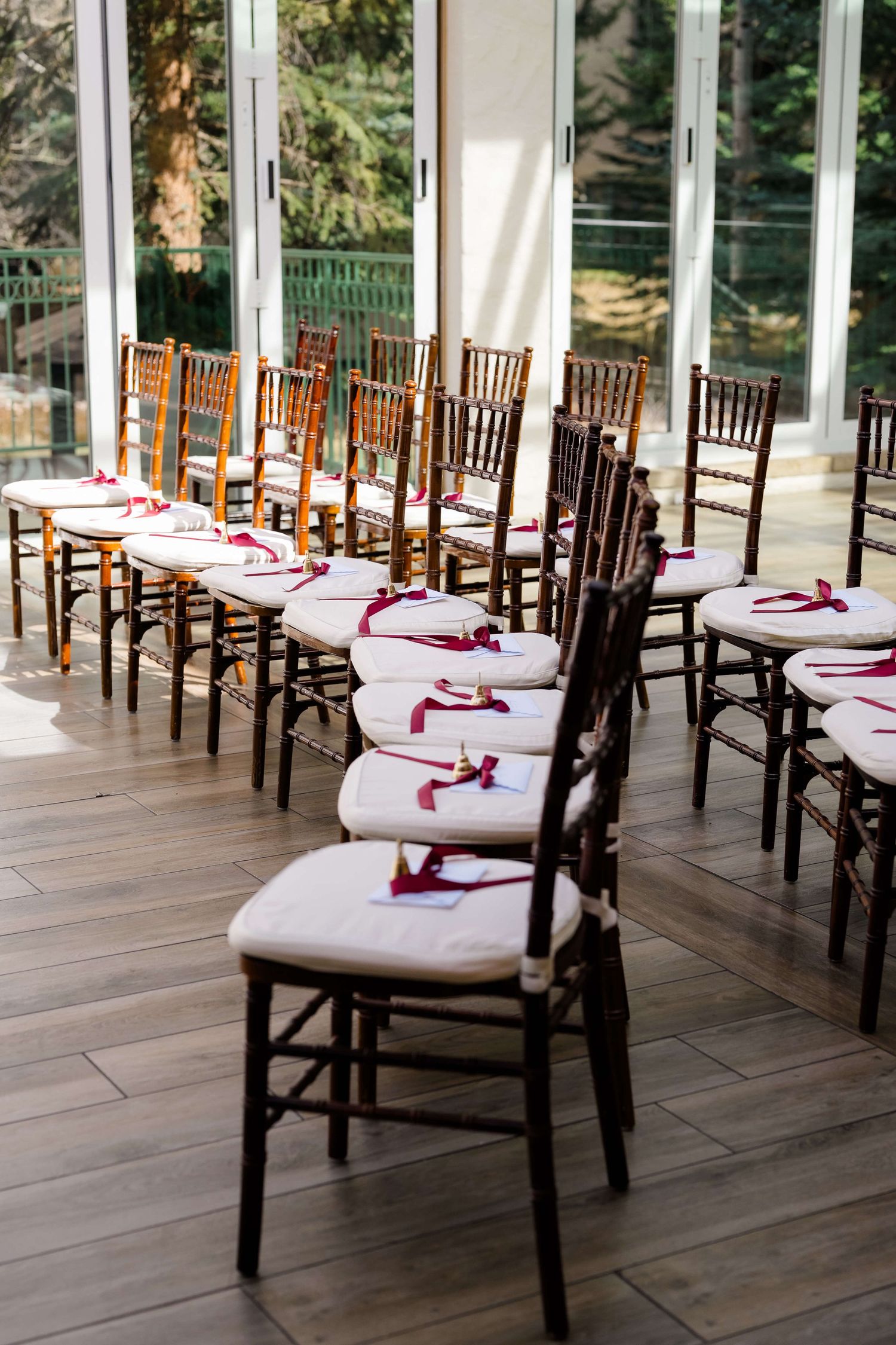 Rows of wooden Chiavari chairs with white cushions and red ribbon accents set up for an elegant indoor wedding ceremony.