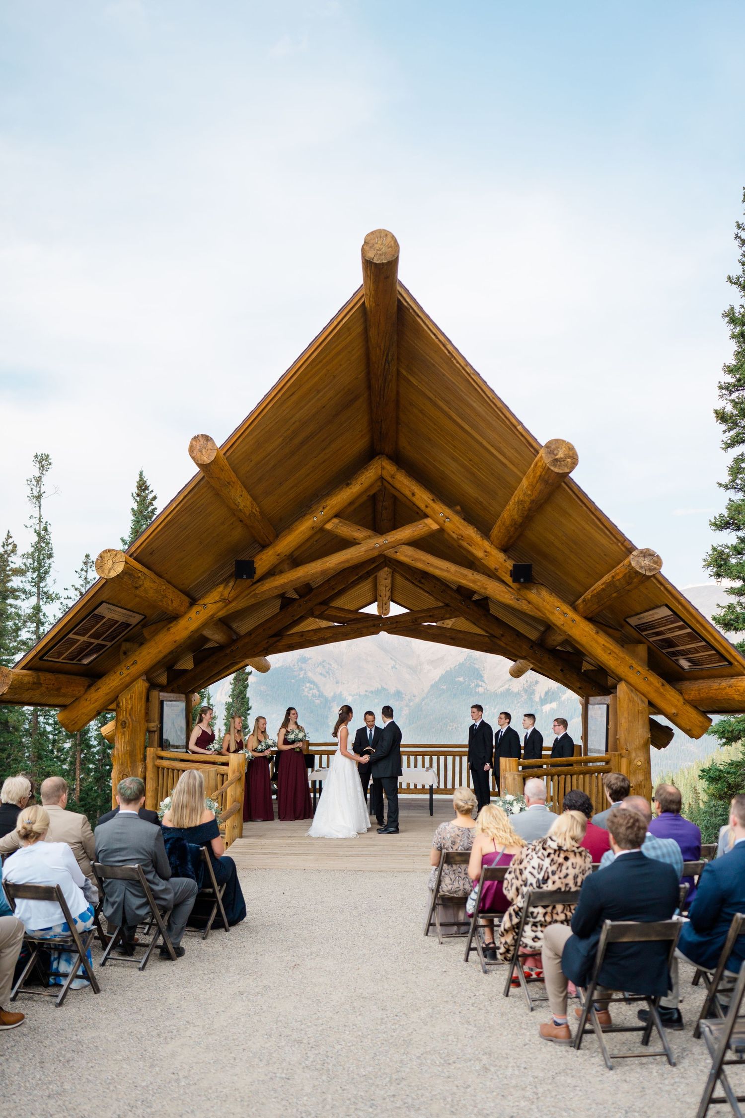 A scenic mountain wedding ceremony takes place under a rustic wooden pavilion with guests seated on folding chairs at aerie at copper.
