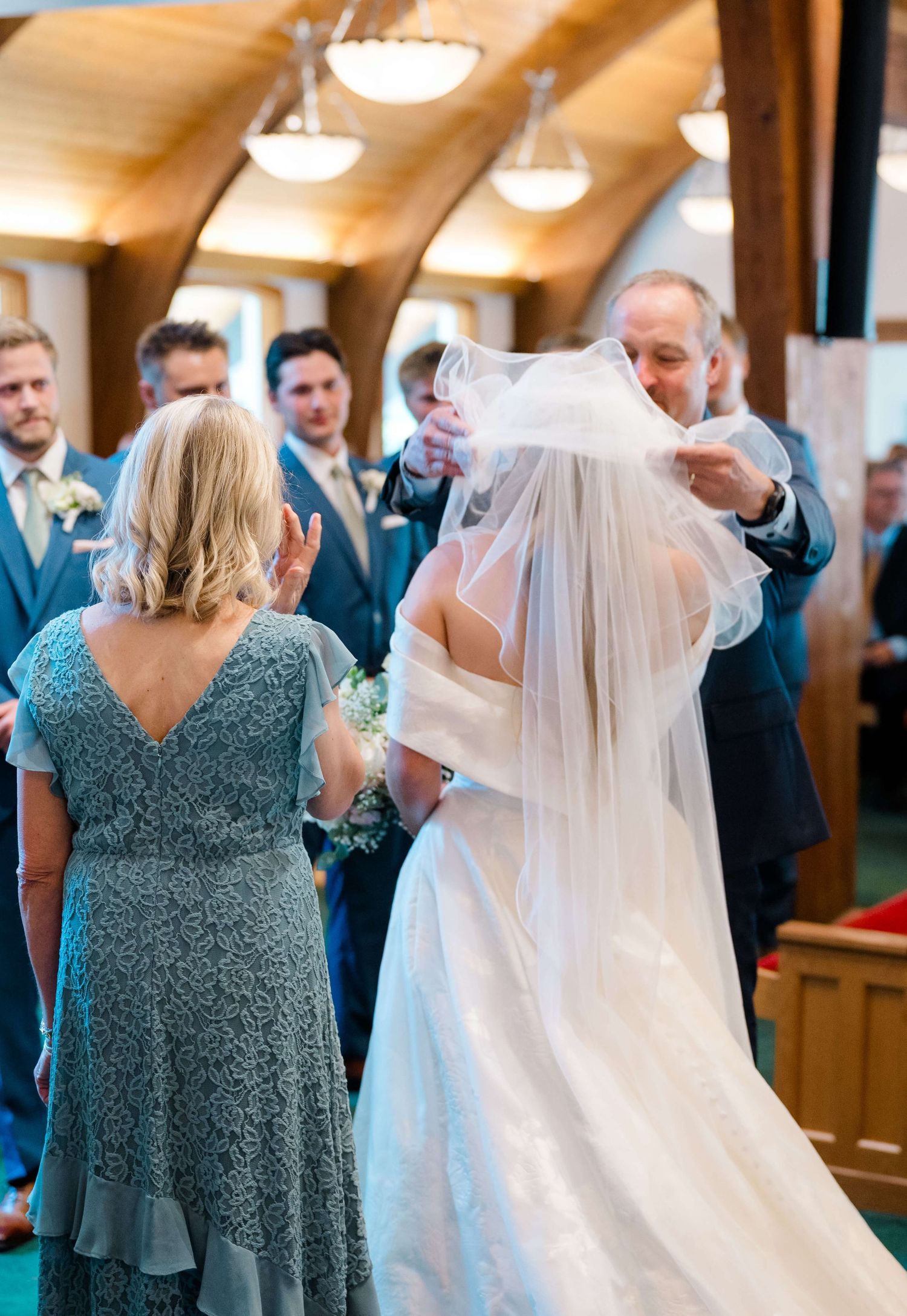 Wedding party in teal bridesmaid dresses and navy suits stands in a rustic venue during ceremony at vail wedding.