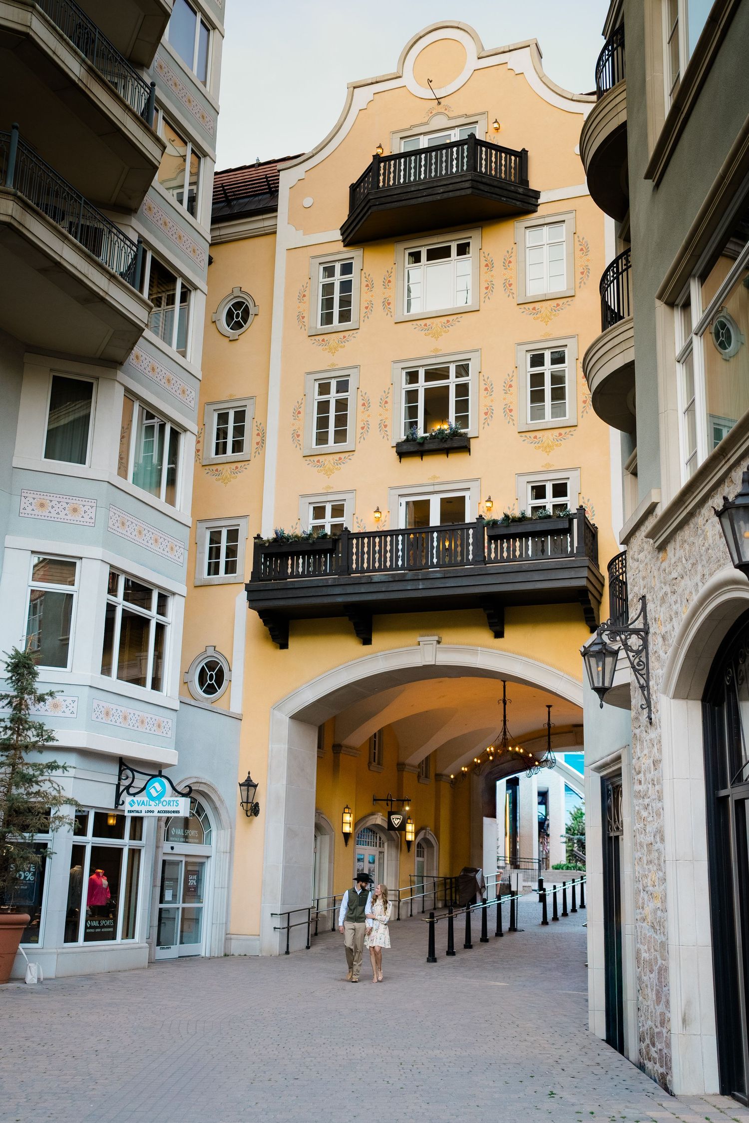 Charming European-style yellow building with arched passageway, balconies, and ornate facade in a pedestrian shopping area.