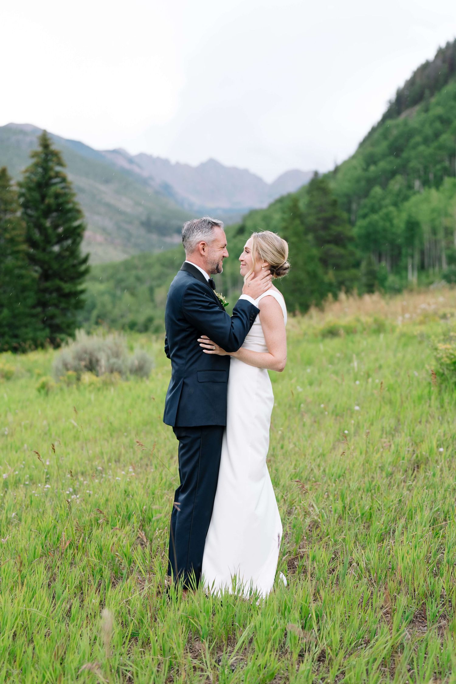 At Vail Golf Club Wedding - Bride and groom embrace in a lush green mountain meadow, sharing a romantic moment in their wedding attire.