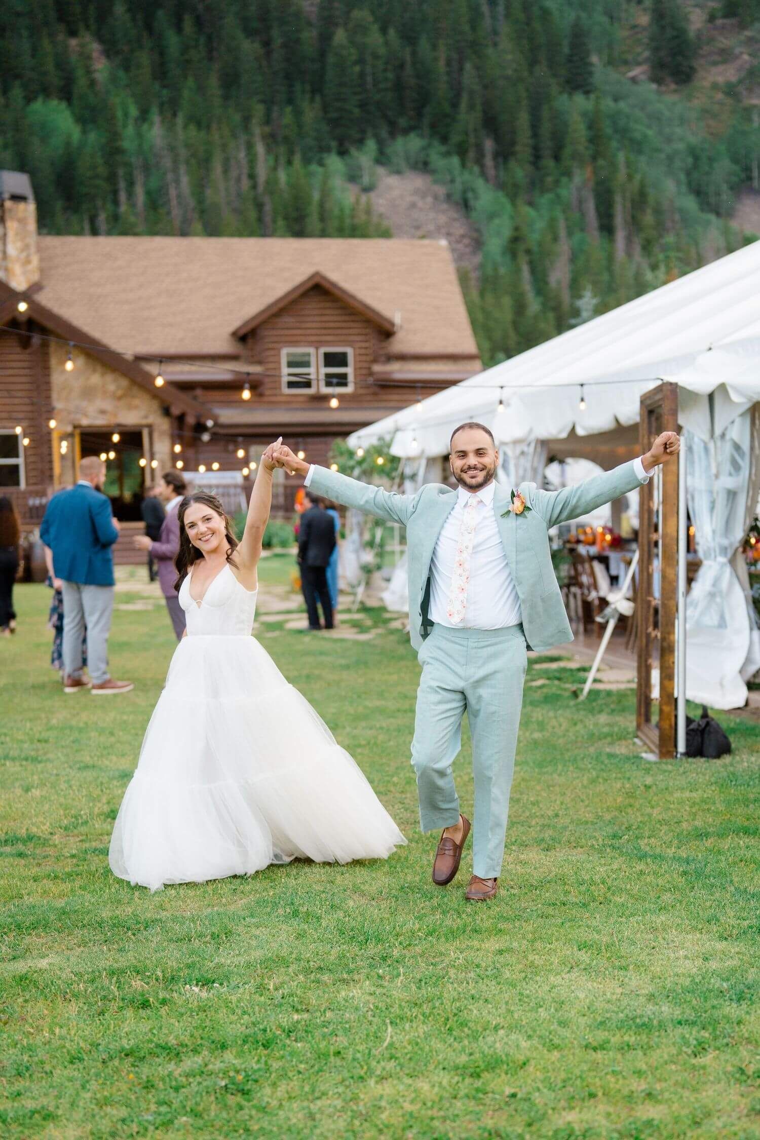 Camp Hale Wedding celebration on a grassy lawn with rustic wooden lodge and white tents in mountain setting.