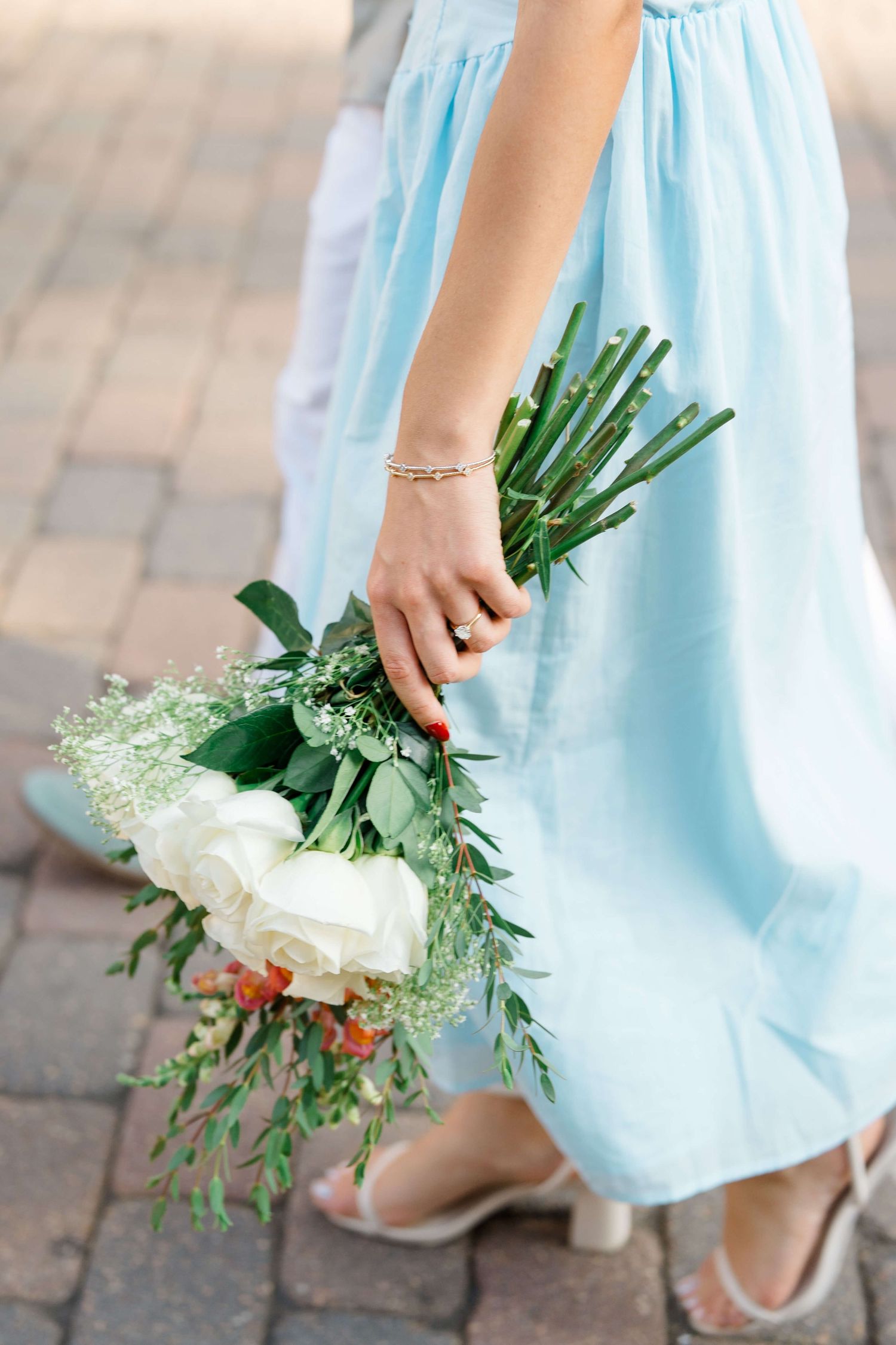 photo showing hands holding a delicate bouquet of white flowers against a light blue dress and brick pavement as vail village proposal