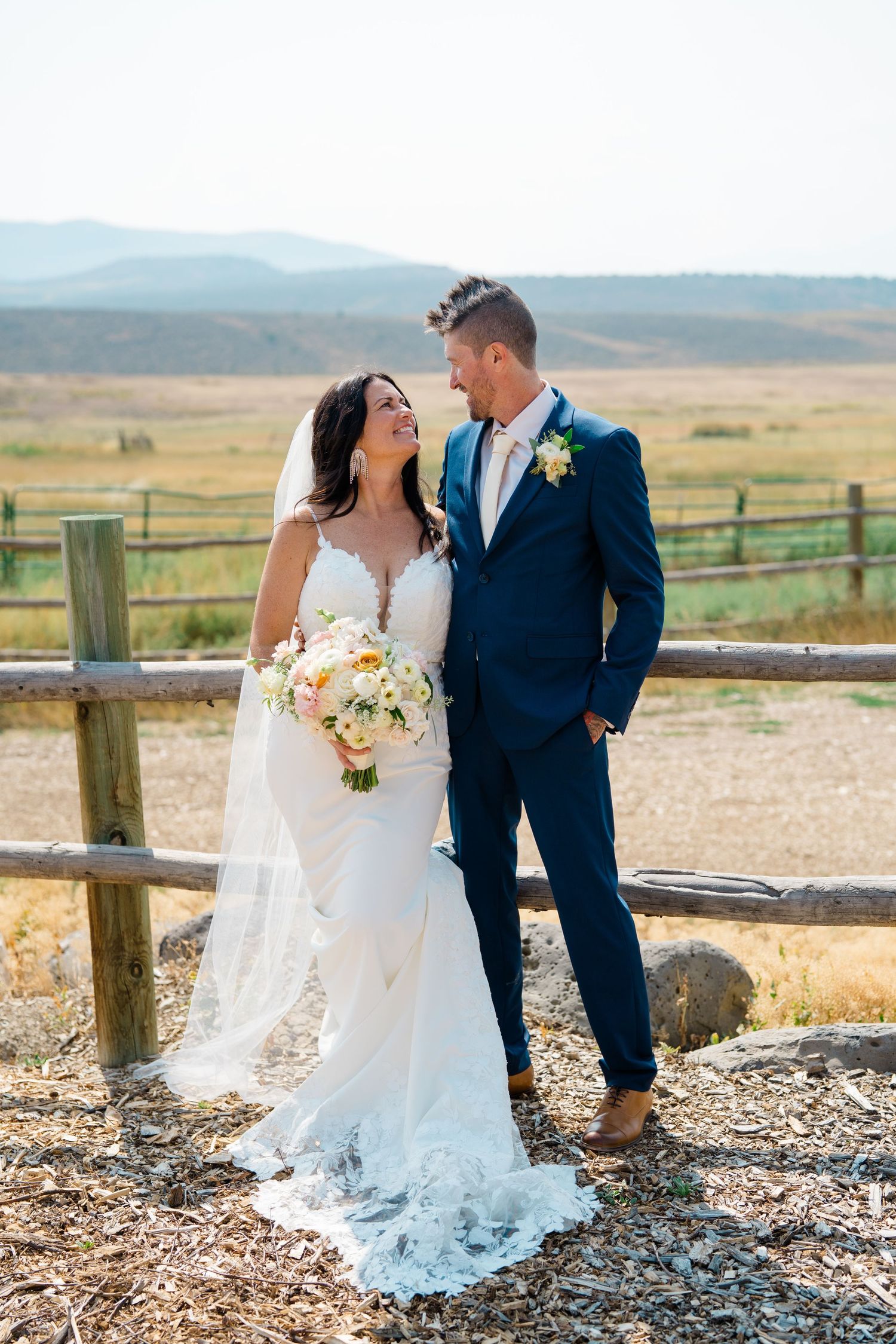 Romantic wedding couple shares intimate moments against rustic mountain backdrop with wooden fence at sunset.