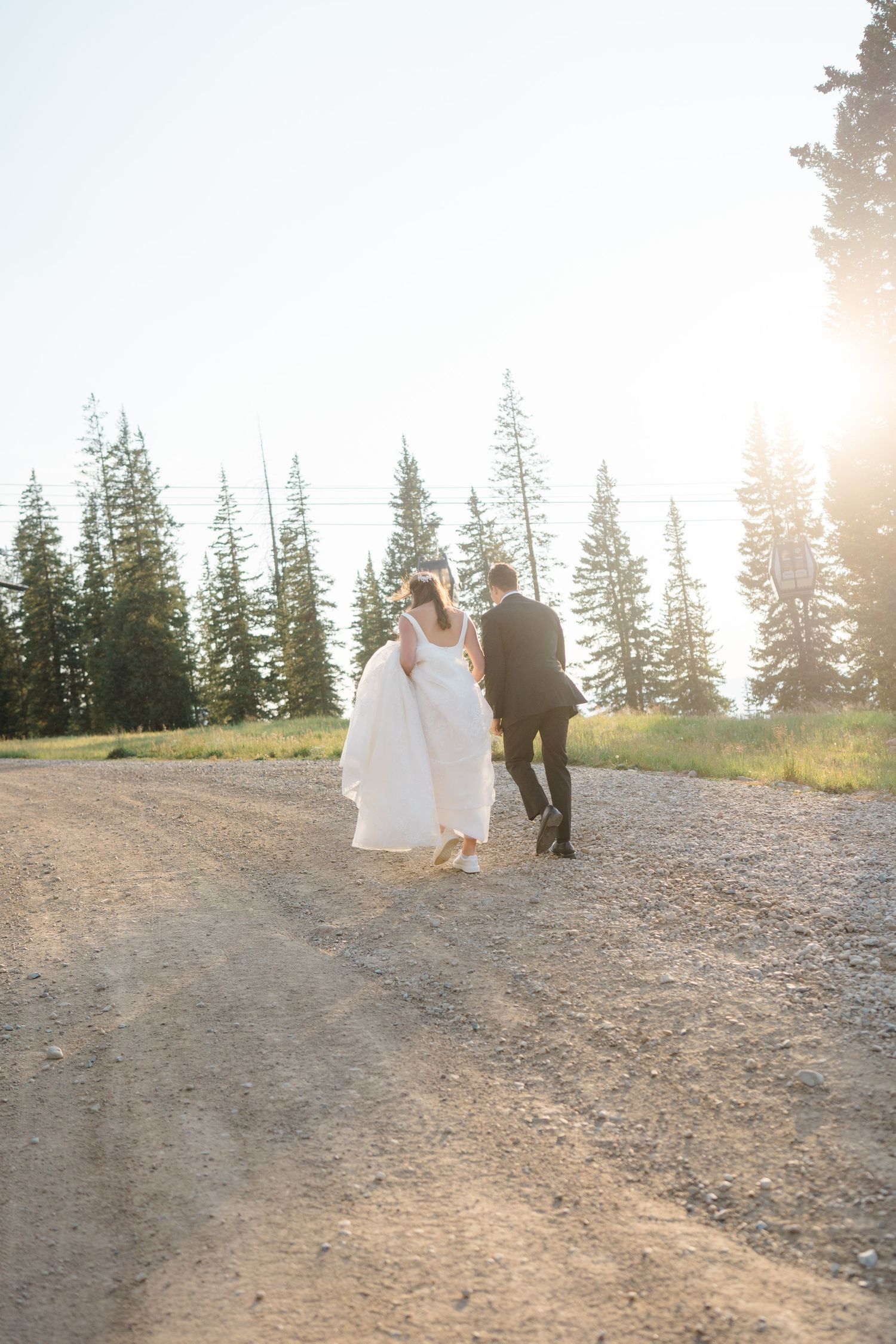Newlyweds walk hand in hand along a mountain trail at sunset with evergreen trees in the background at copper mountain.