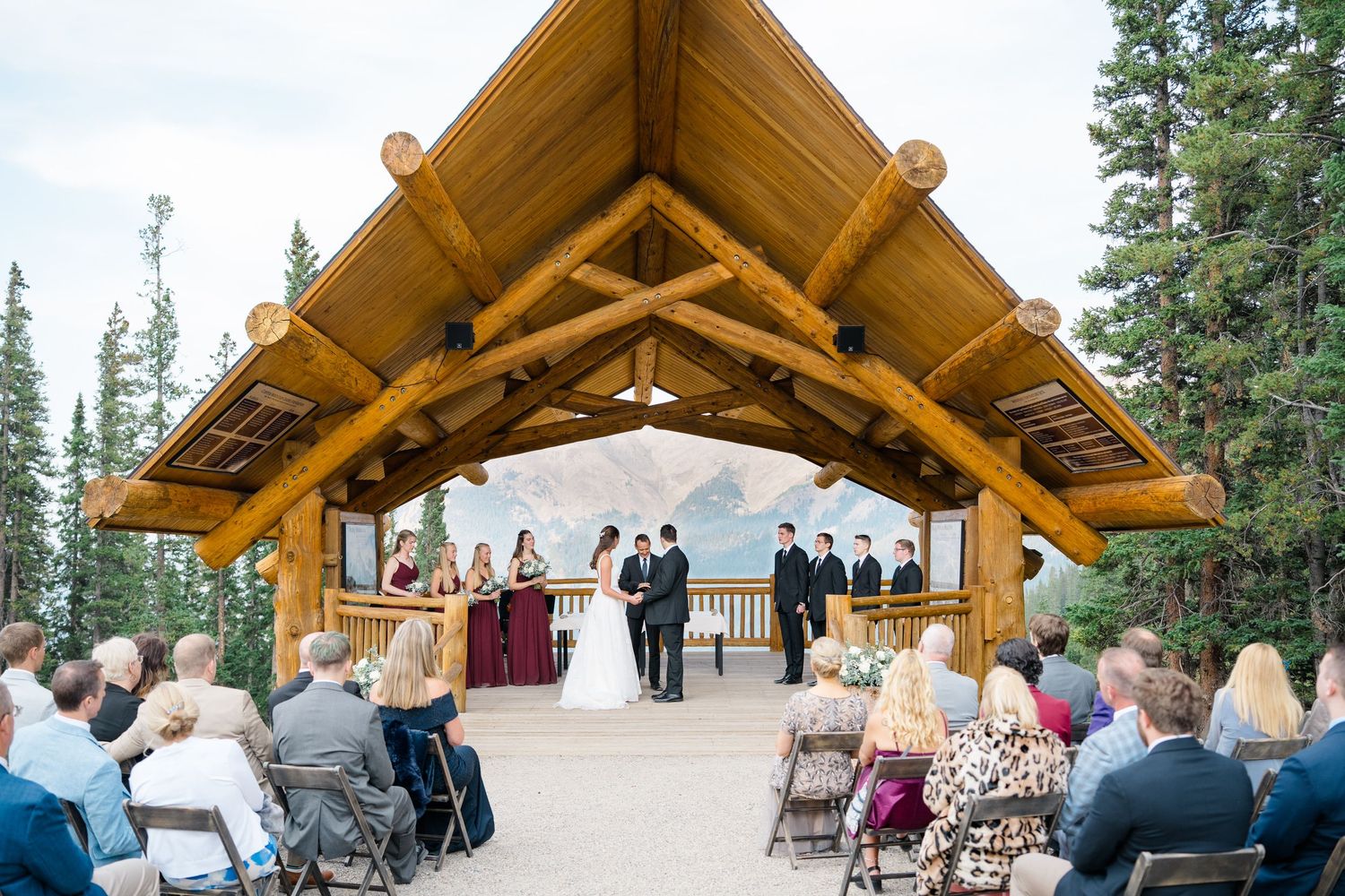 Wedding guests seated under rustic timber pavilion with mountain views during outdoor ceremony at copper mountain.