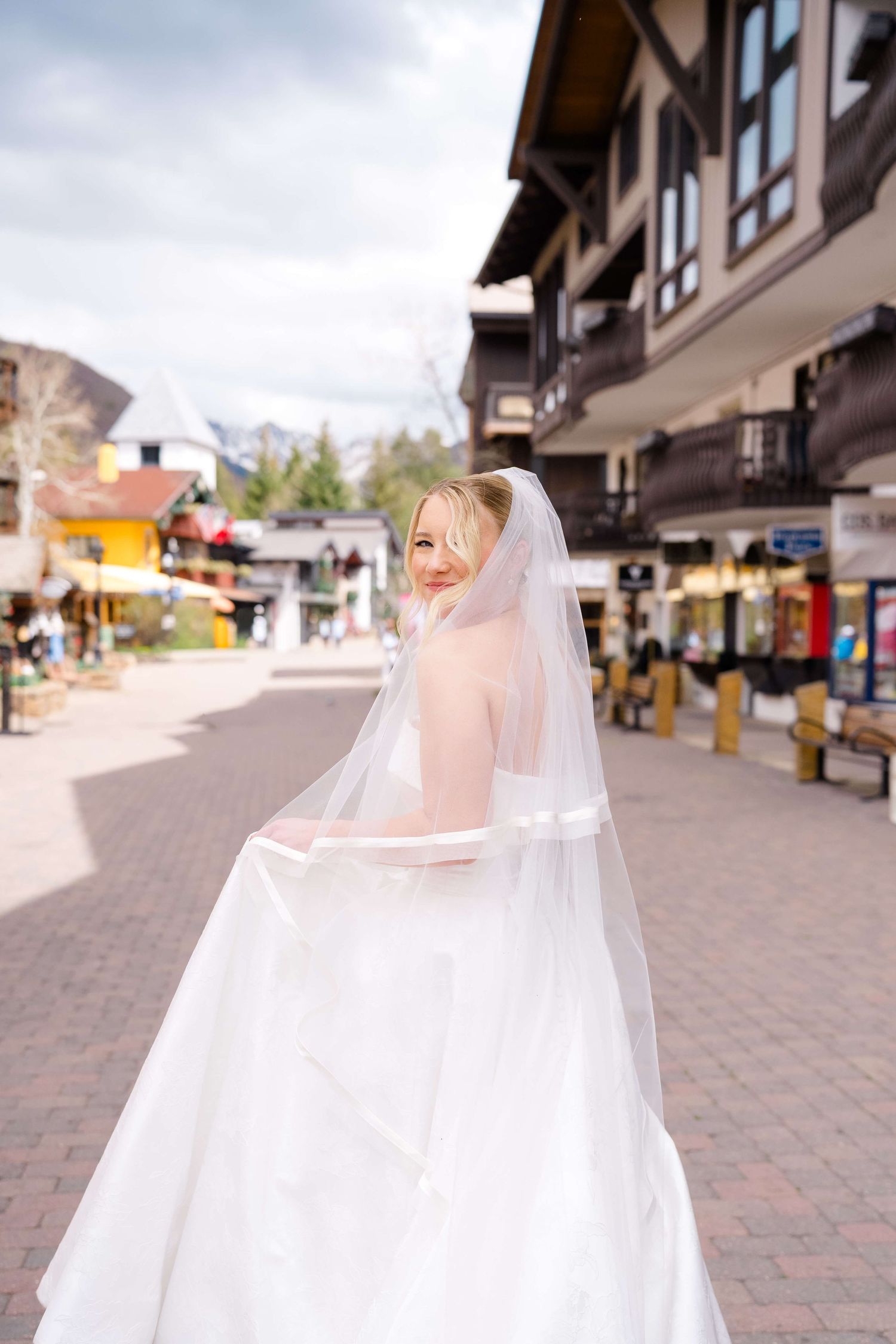 Smiling bride in a white wedding gown and veil walking through a charming mountain town village street.
