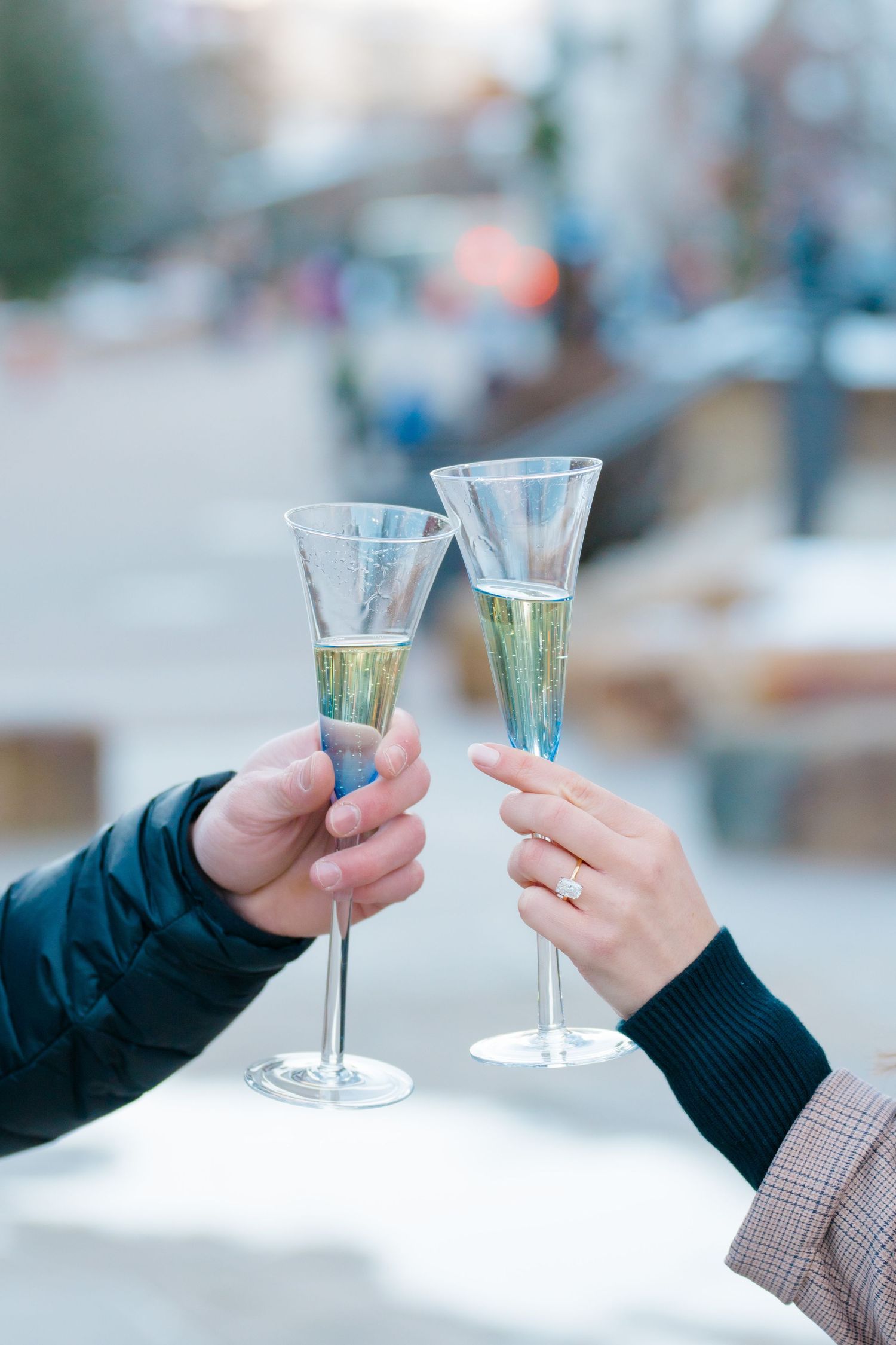 Two hands holding champagne glasses toasting together in a celebratory moment against a blurred background.