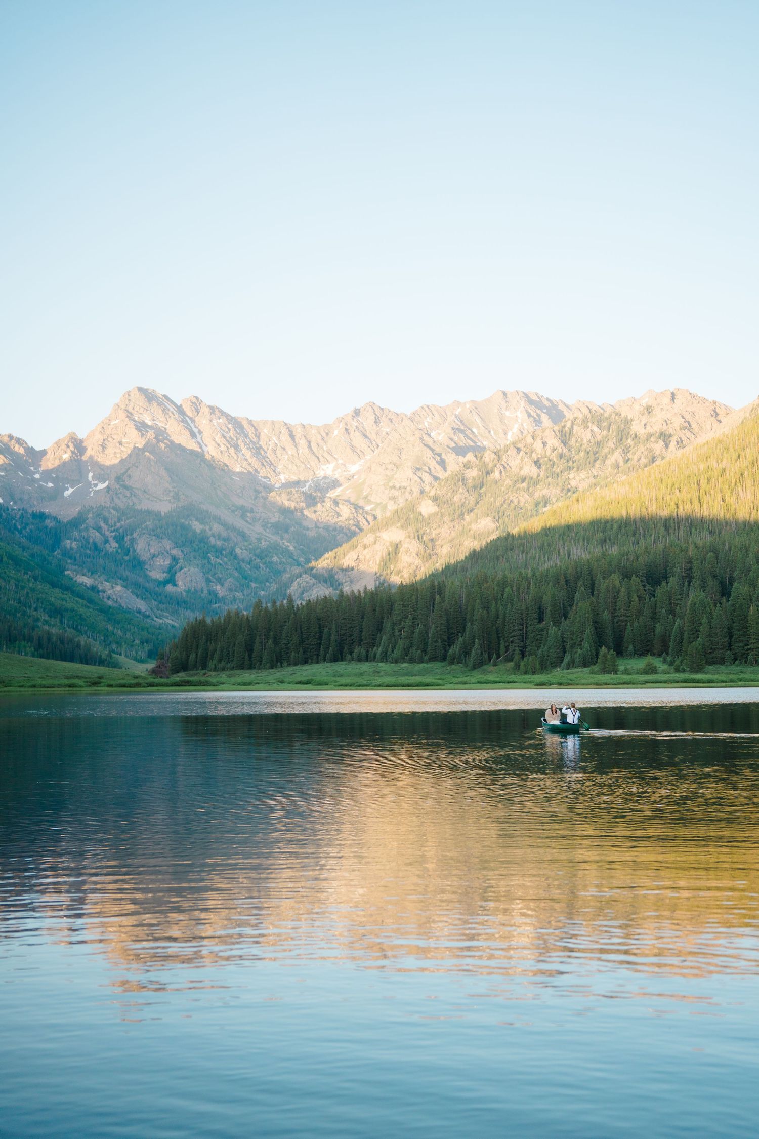 Scenic mountain lake view with evergreen forests and snow-capped peaks reflecting in calm waters at sunset in vail, colorado wedding.