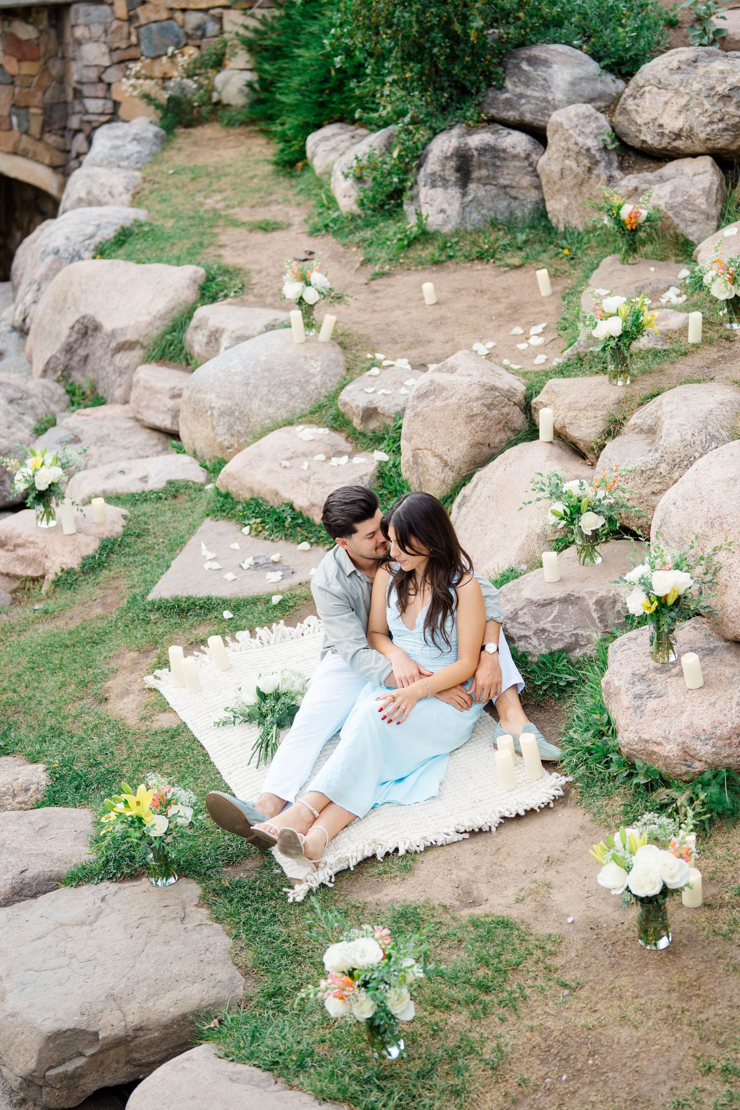 An intimate picnic setup with white blankets and floral decorations arranged near large natural boulders.