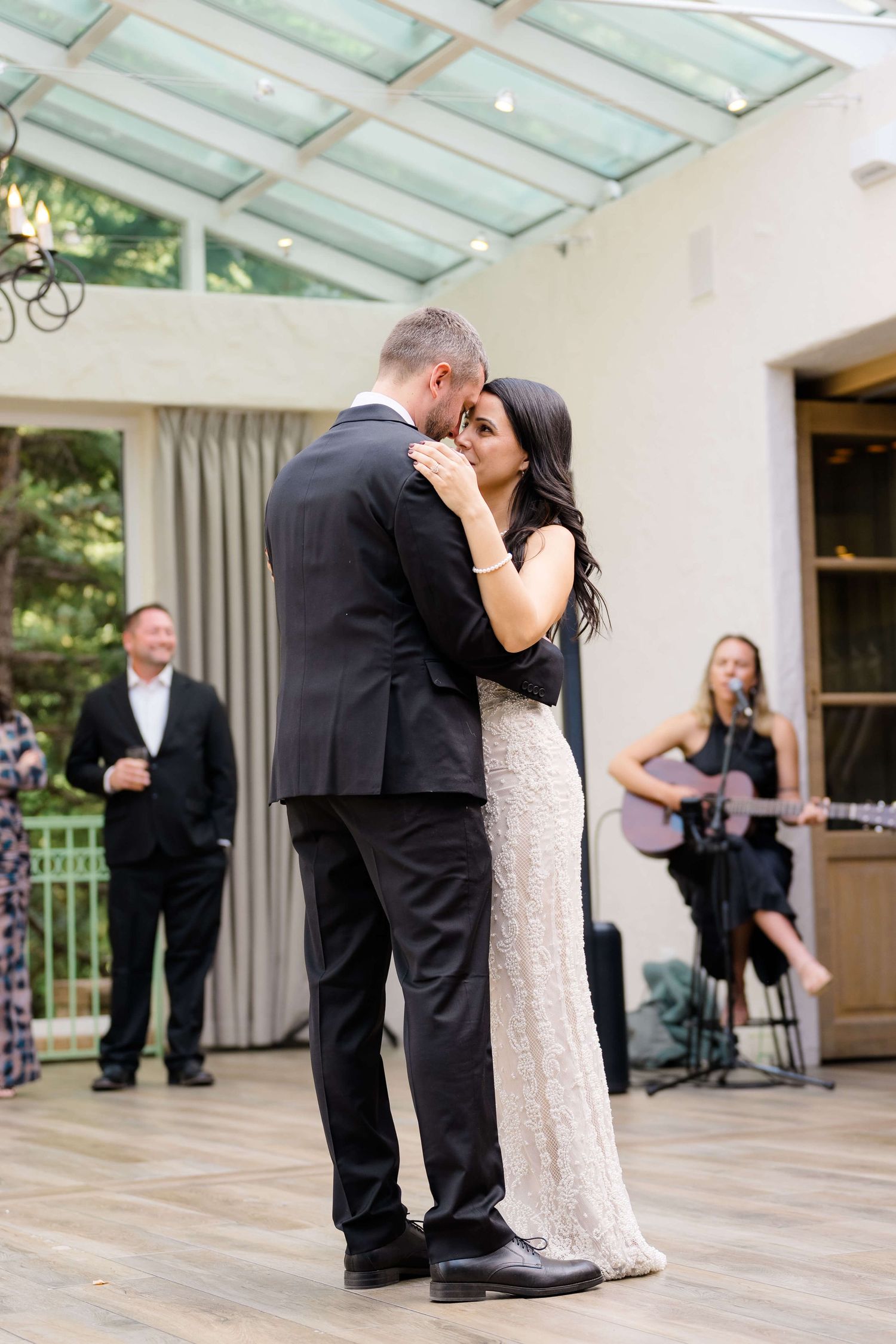 Couple shares their first dance at wedding reception while guitarist performs live music in elegant venue.